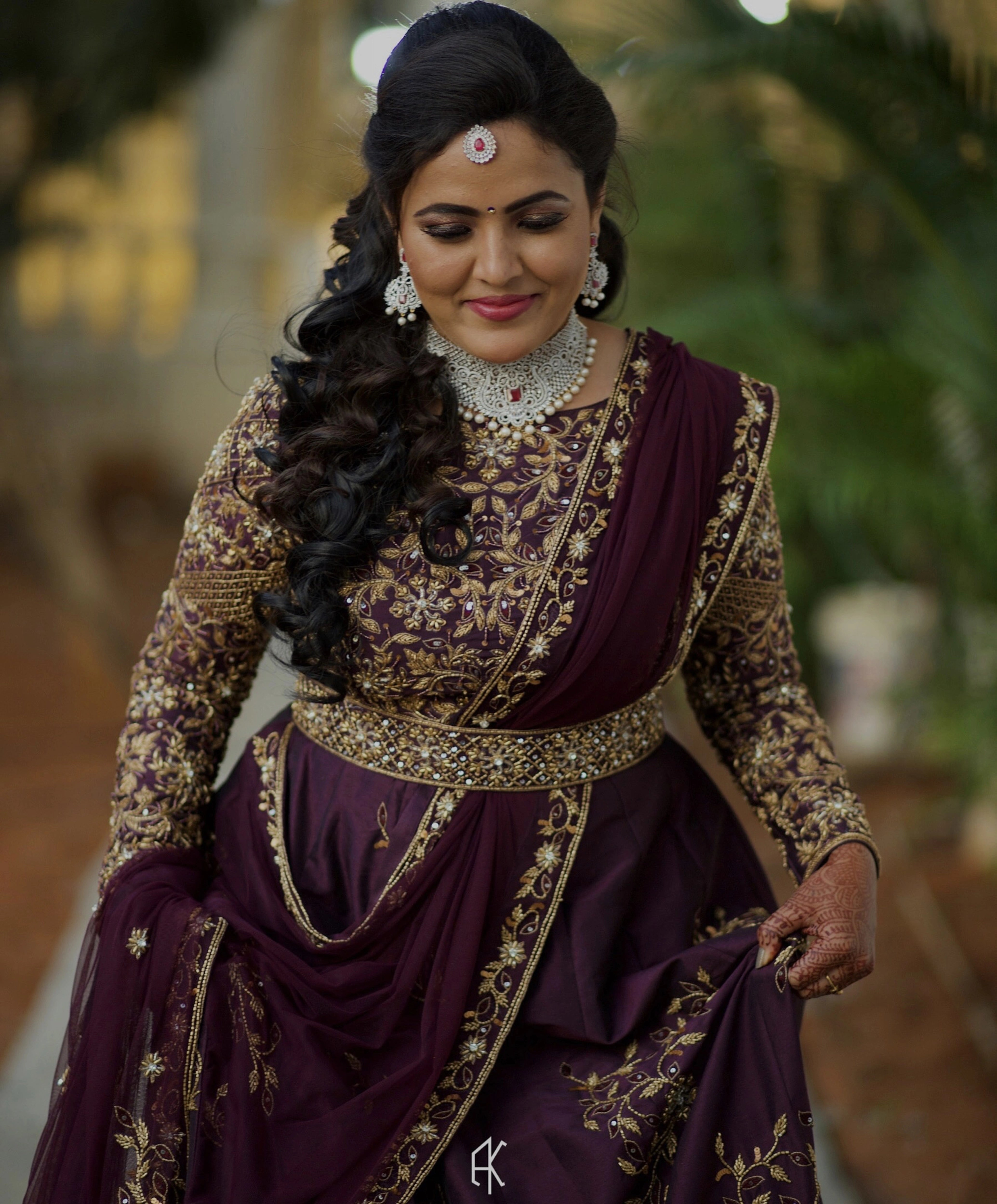 Bride Deepika smiling in an eggplant colored raw silk draped gown with belt intricately embellished with cutdana, sequins, stones and beads by team Archana Karthick.