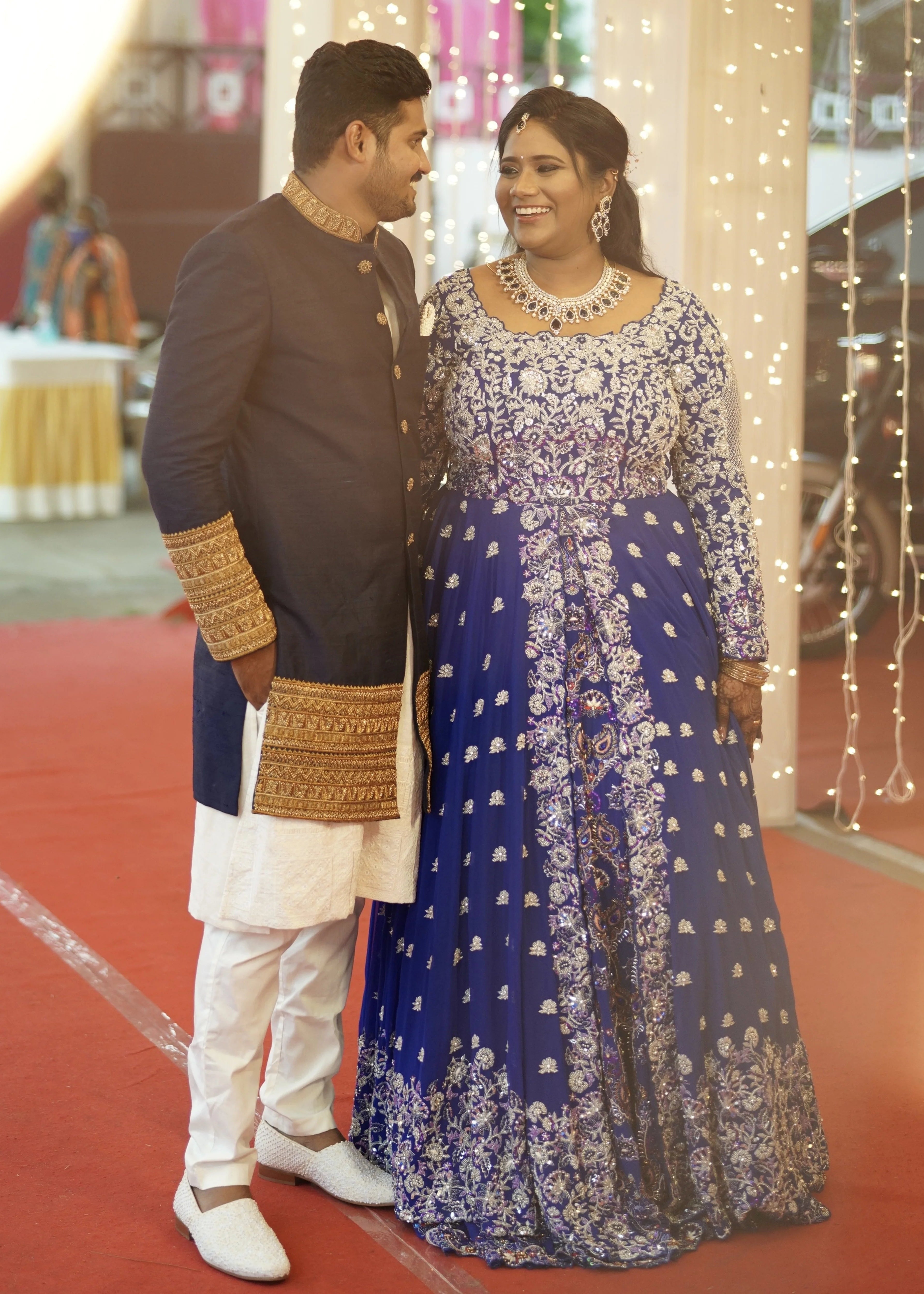 Bride & Groom from Dindigul, hand in hand in a midnight blue handcrafted masakali lehenga and navy blue raw silk sherwani with embellished collar, cuffs and borders. Designed by Archana Karthick
