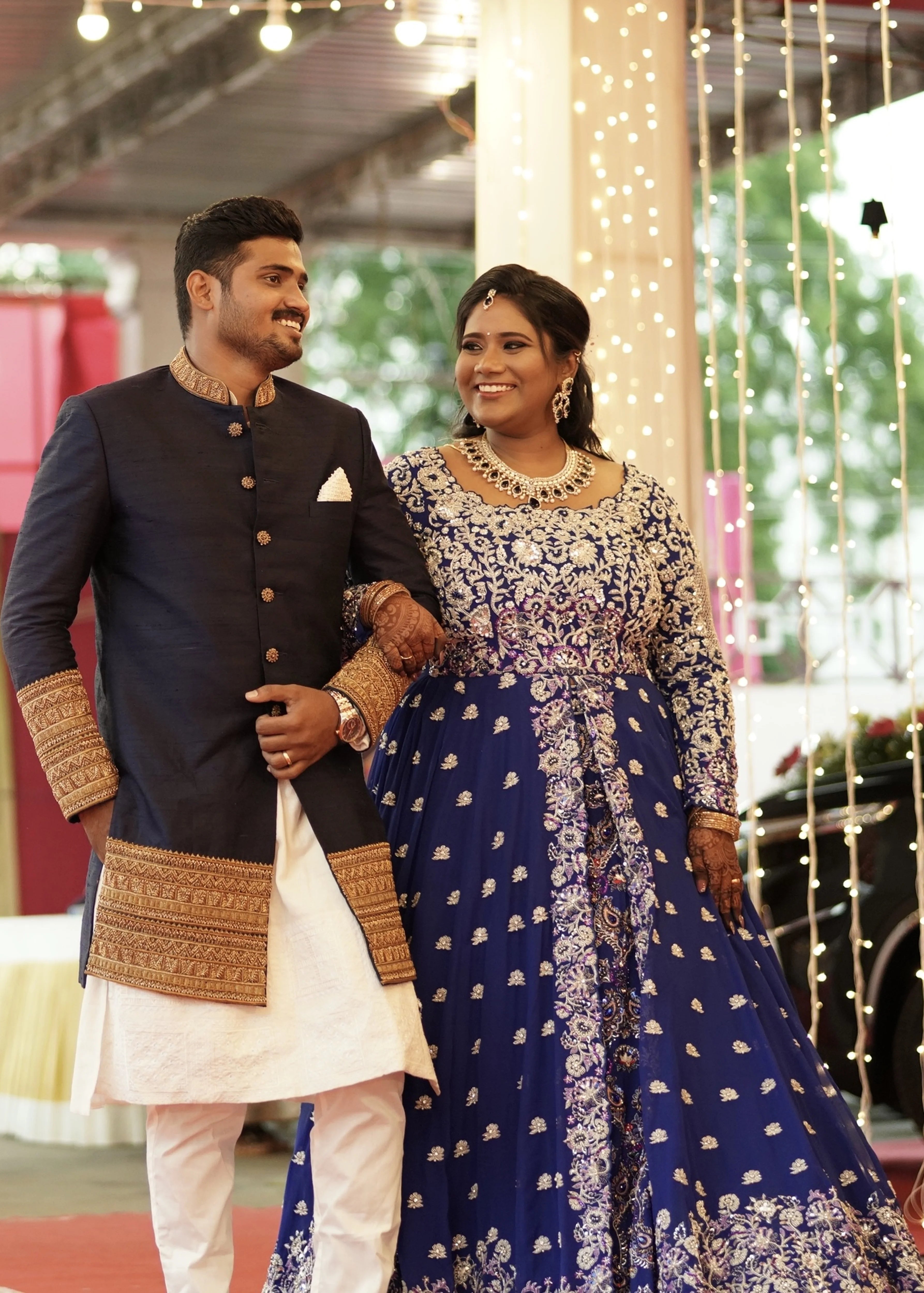 Bride & Groom from Dindigul, smiling in a midnight blue handcrafted masakali lehenga and navy blue raw silk sherwani with embellished collar, cuffs and borders. Designed by Archana Karthick
