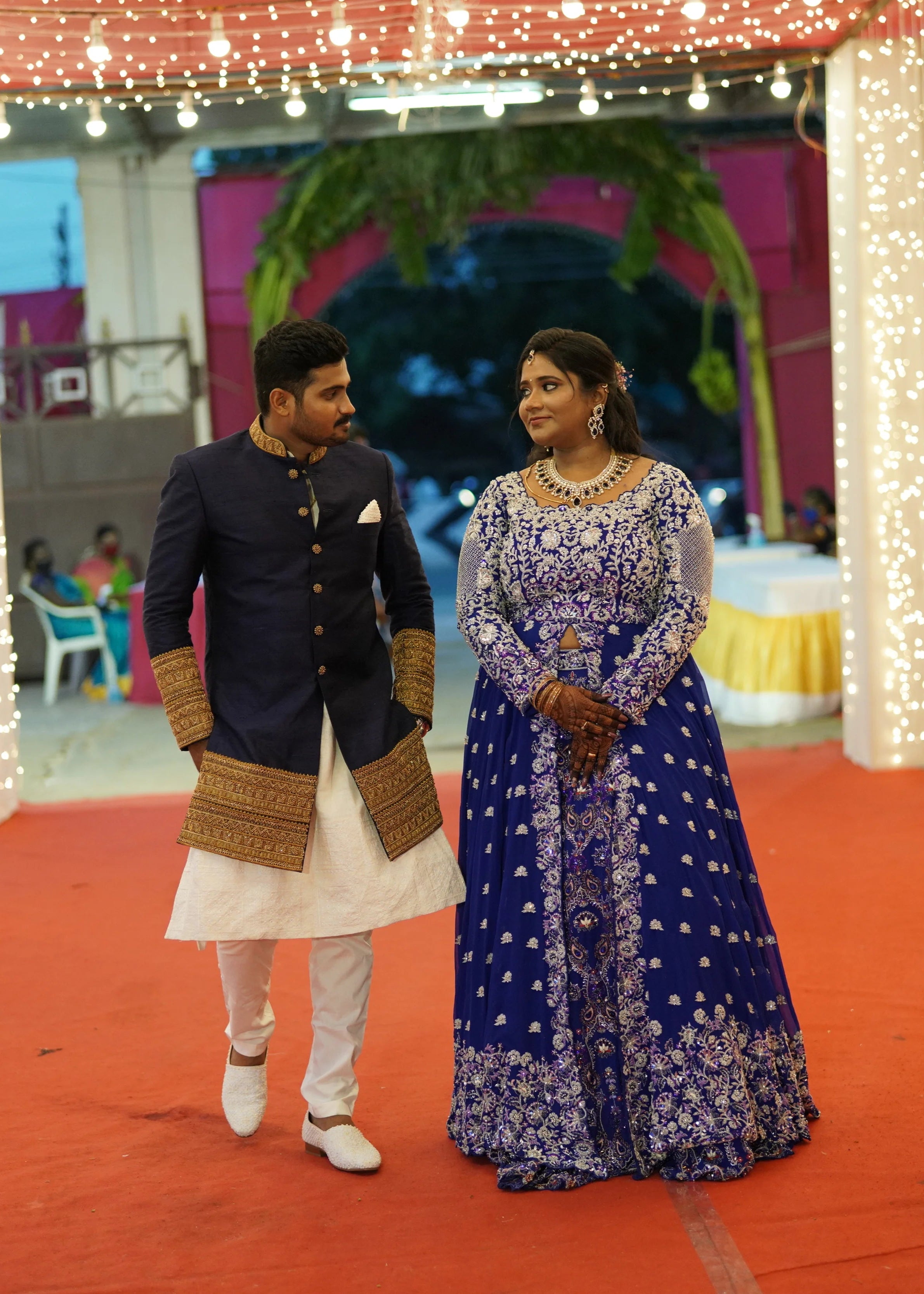Bride & Groom from Dindigul, walking together in a midnight blue handcrafted masakali lehenga and navy blue raw silk sherwani with embellished collar, cuffs and borders. Designed by Archana Karthick