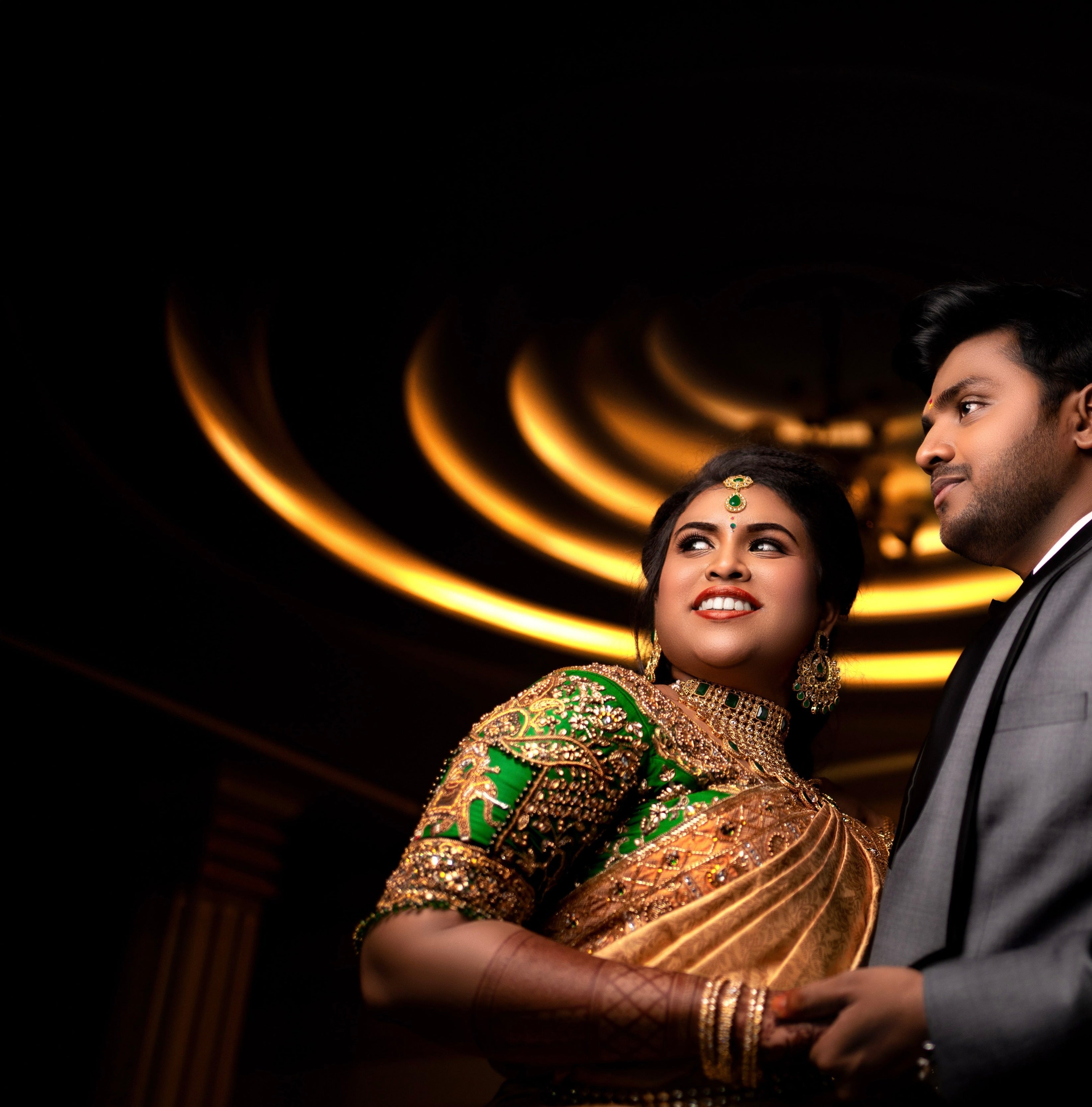 Bride Hemakiruthika from Chennai in a green raw silk blouse and gold silk saree with heavy border embellishments, designed by Archana Karthick. She is looking to her right and is posing looking to her right for an intimate smile.