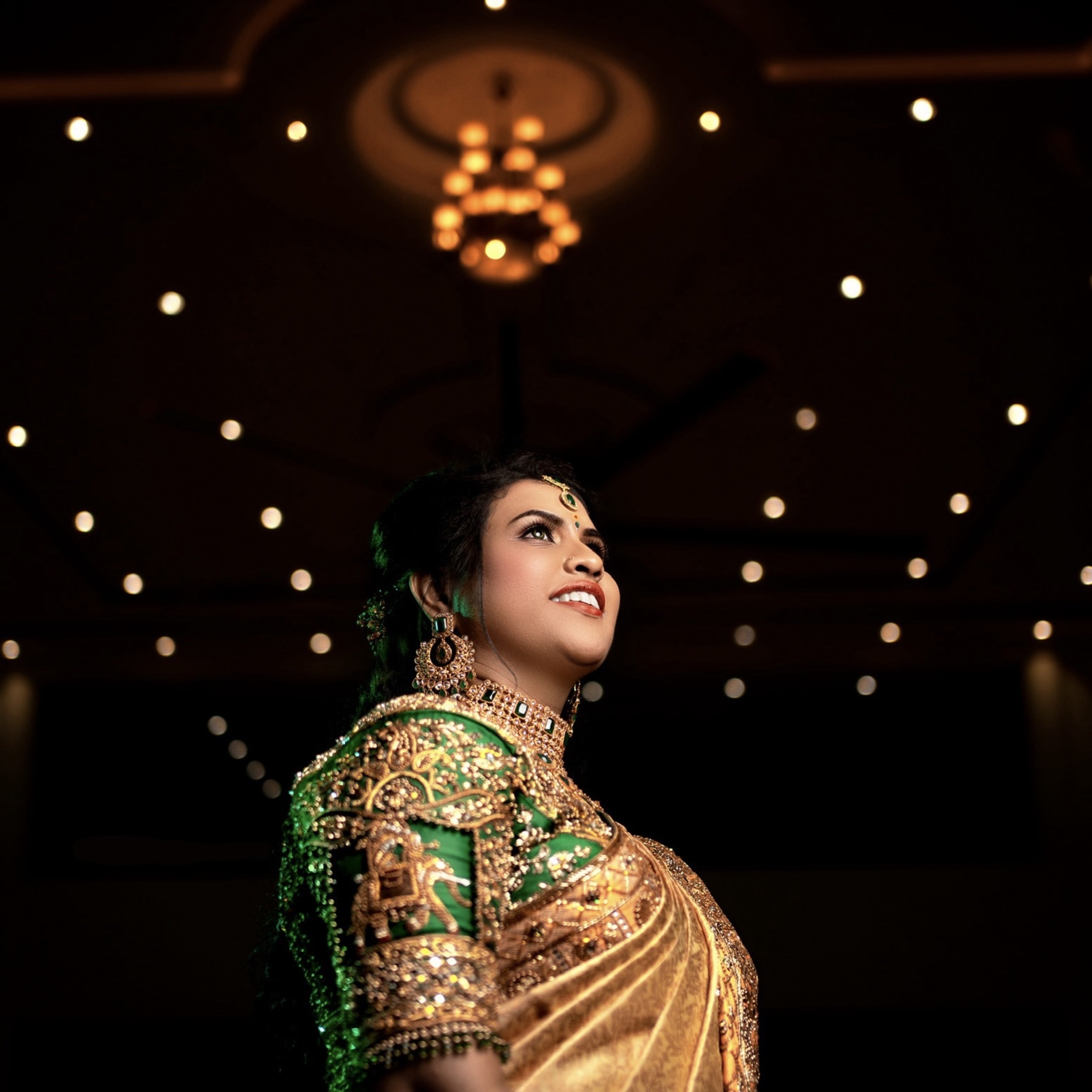 Bride Hemakiruthika from Chennai in a green raw silk blouse and gold silk saree with heavy border embellishments, designed by Archana Karthick. She is looking away and her sleeve has been captured.