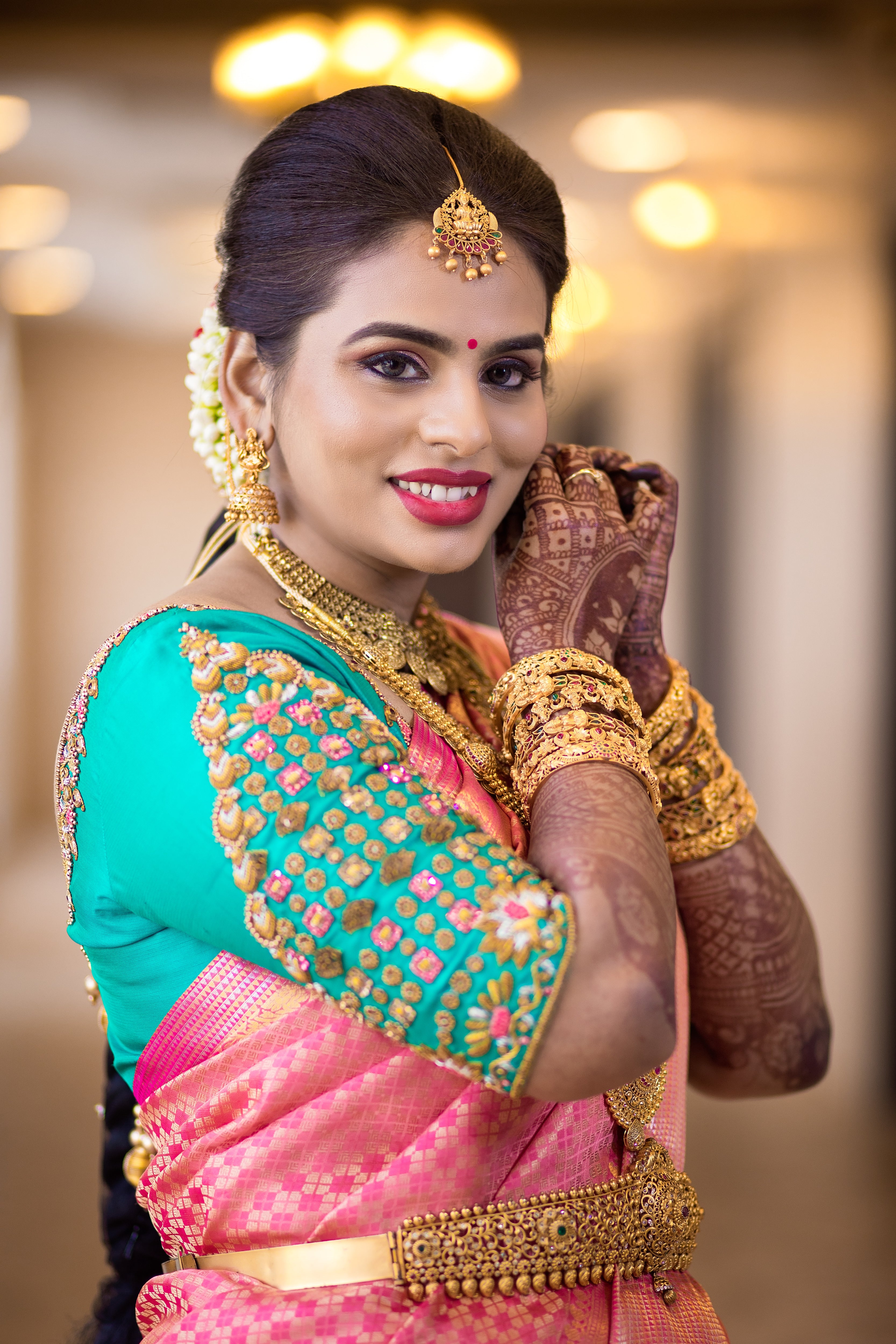 Bride Kowsalya from USA in a teal raw silk blouse designed by Archana Karthick. Posing wearing her ear rings.