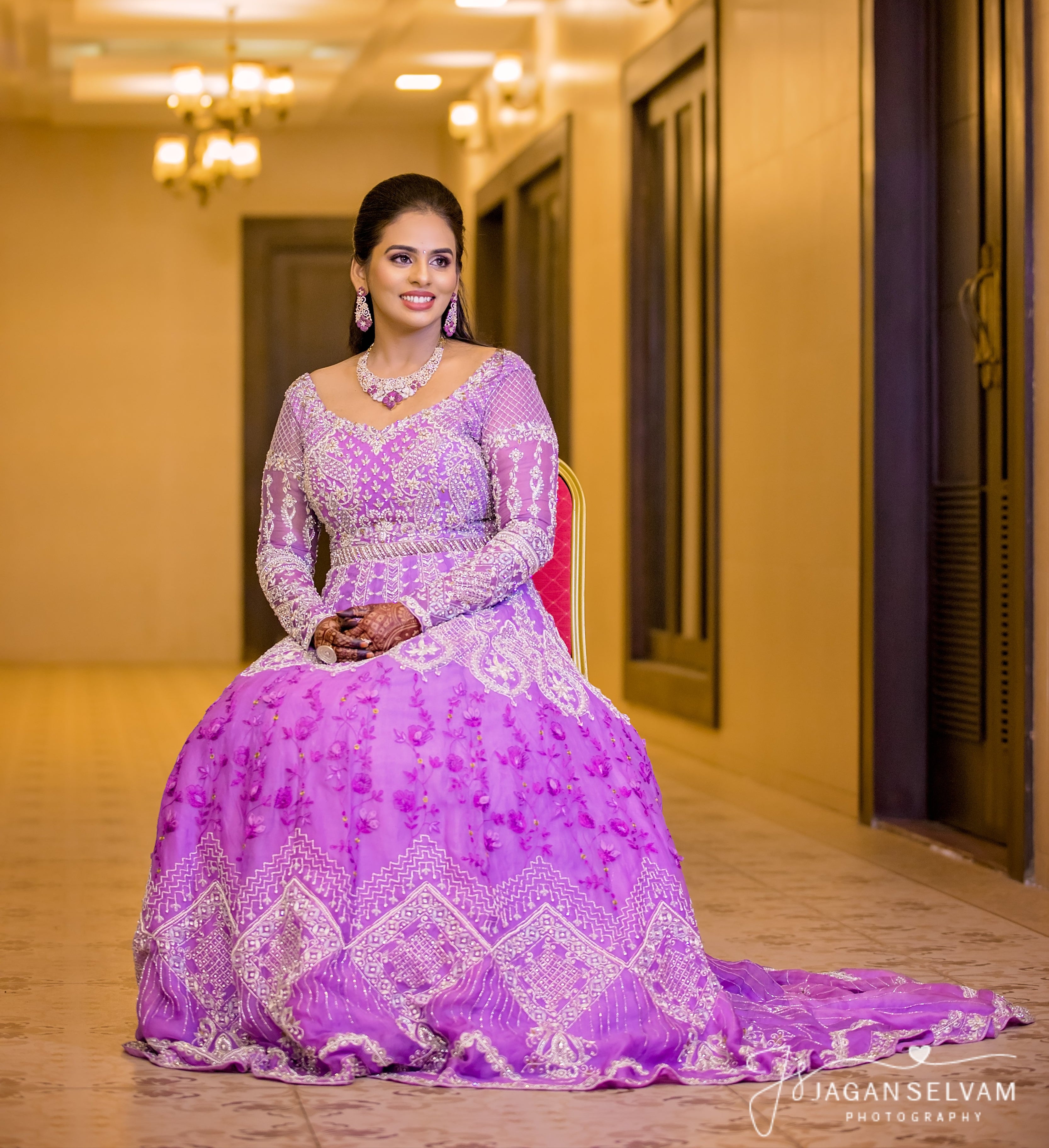 Bride Kowsalya in handcrafted lavender bridal gown designed by Archana Karthick. Seated straight at the camera full profile.