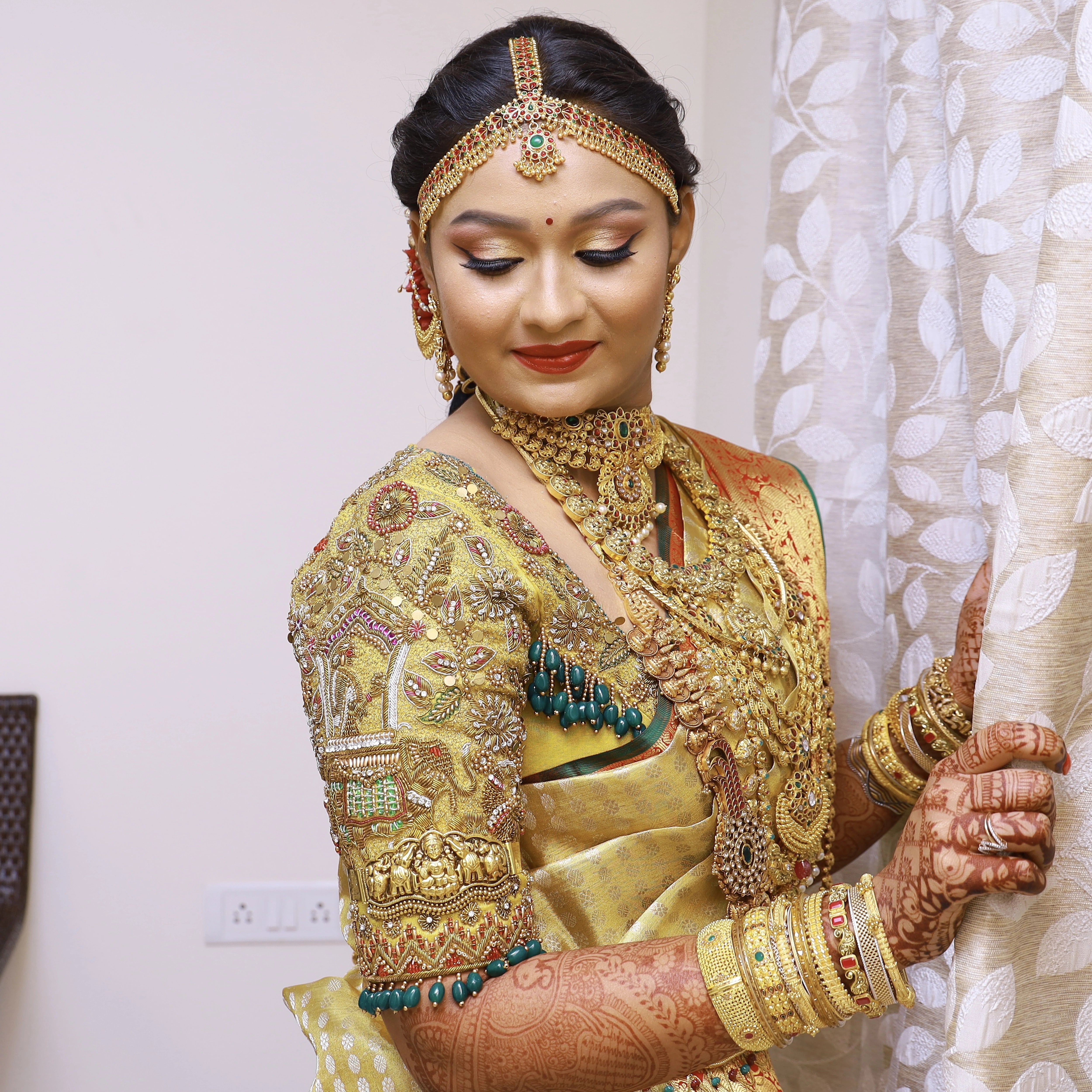 Bride Krithika Balan smiling in gold silk palanquin concept blouse, intricately handcrafted with zardozi, coins, resham, kemp stones and beads by team Archana Karthick.