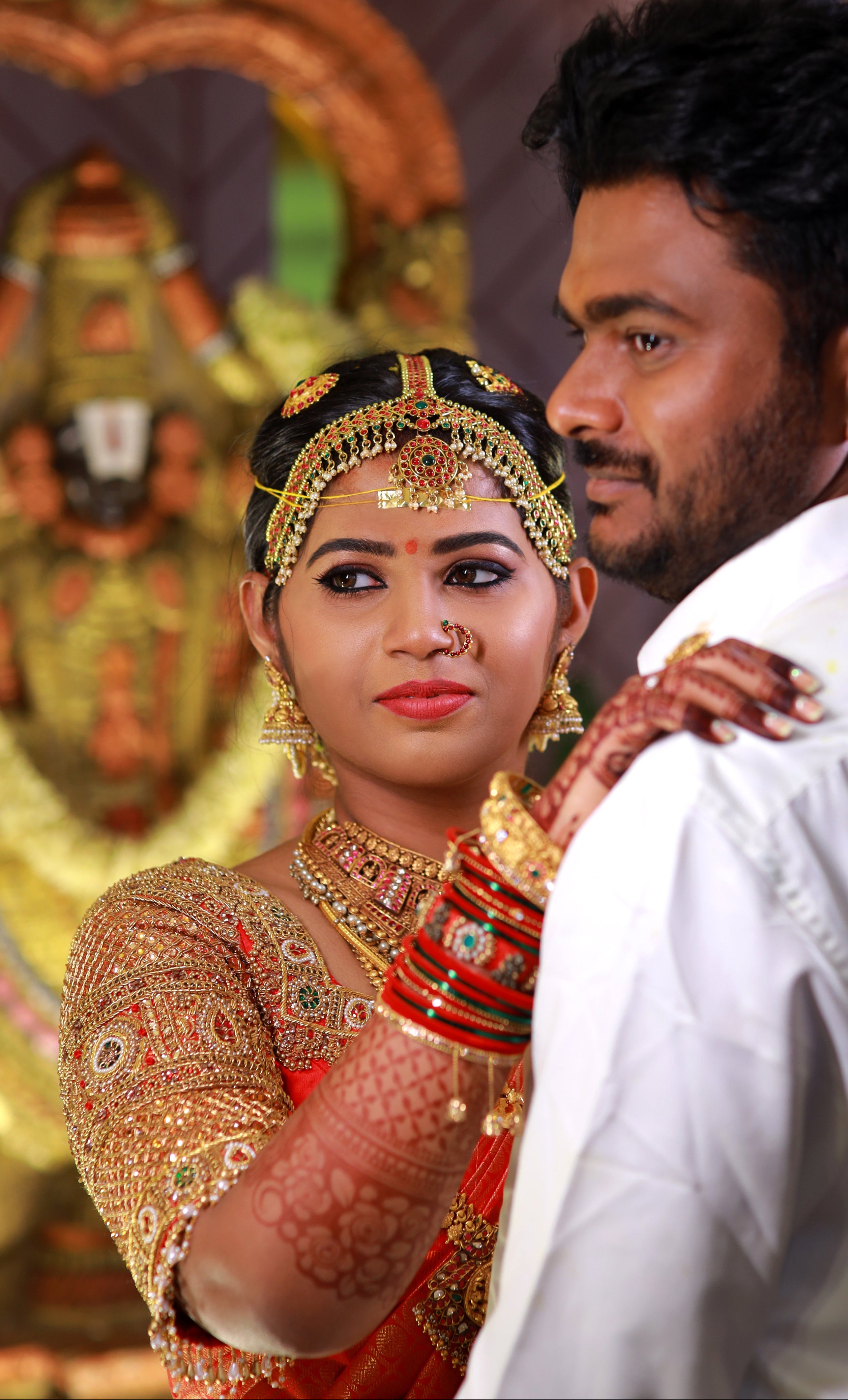 Bride Madhuvarshini in a handcrafted bridal red silk blouse designed by Archana Karthick. Posing with her hand on groom's shoulder.
