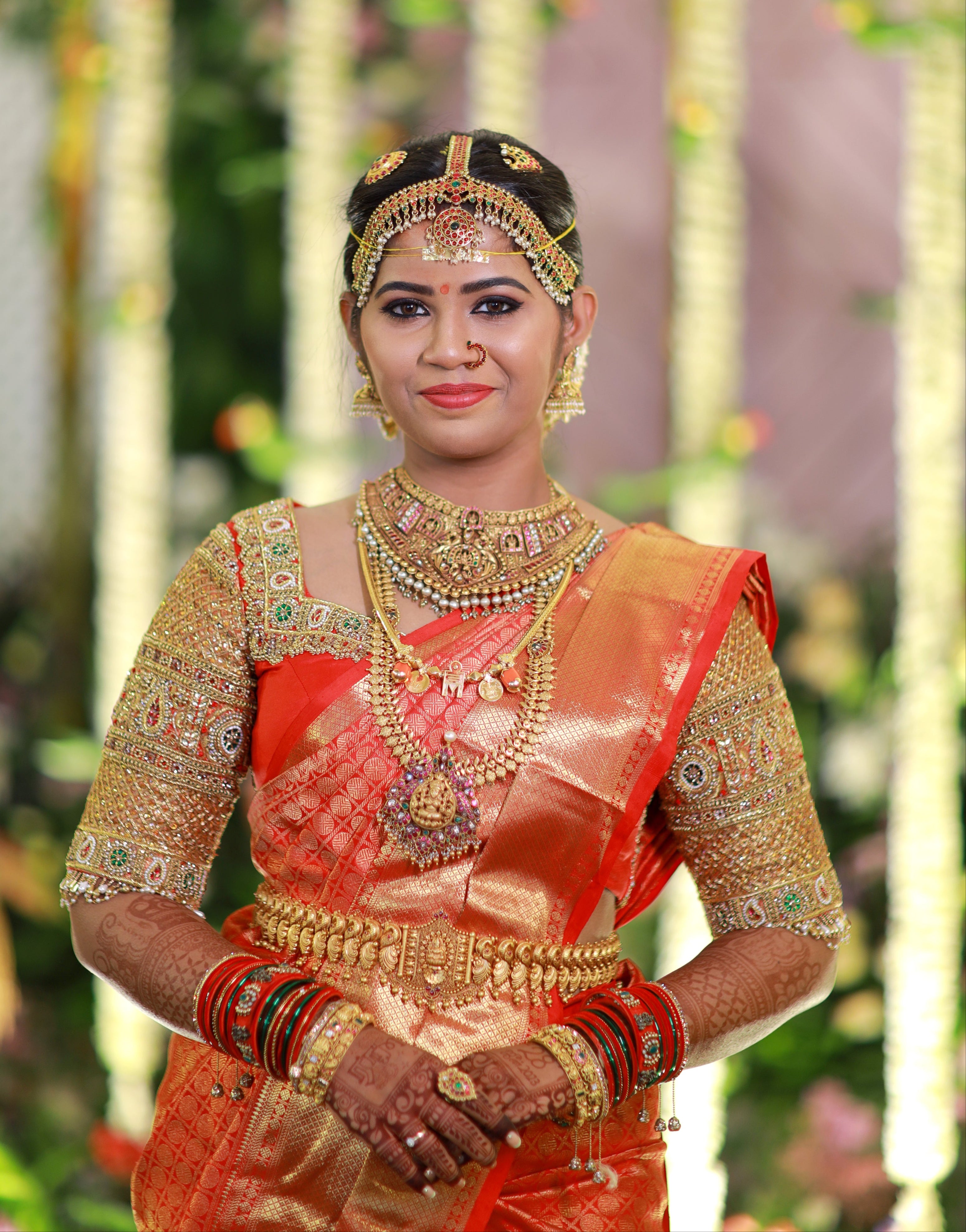 Bride Madhuvarshini in a handcrafted bridal red silk blouse designed by Archana Karthick. Smiling straight at the camera.