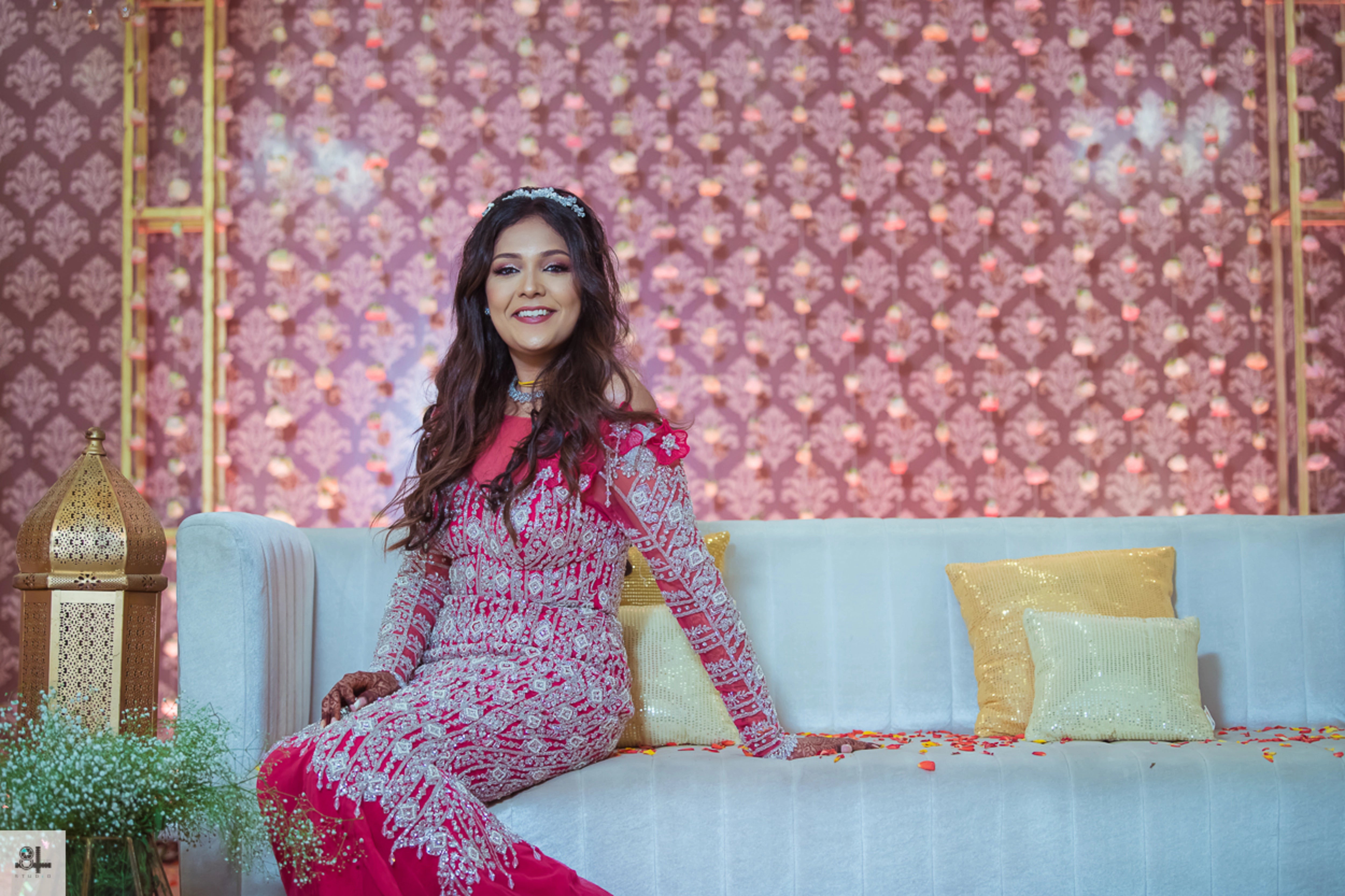 Bride Maygha Viswanath from UK posing on sofa in a hot pink mermaid gown by team Archana Karthick.