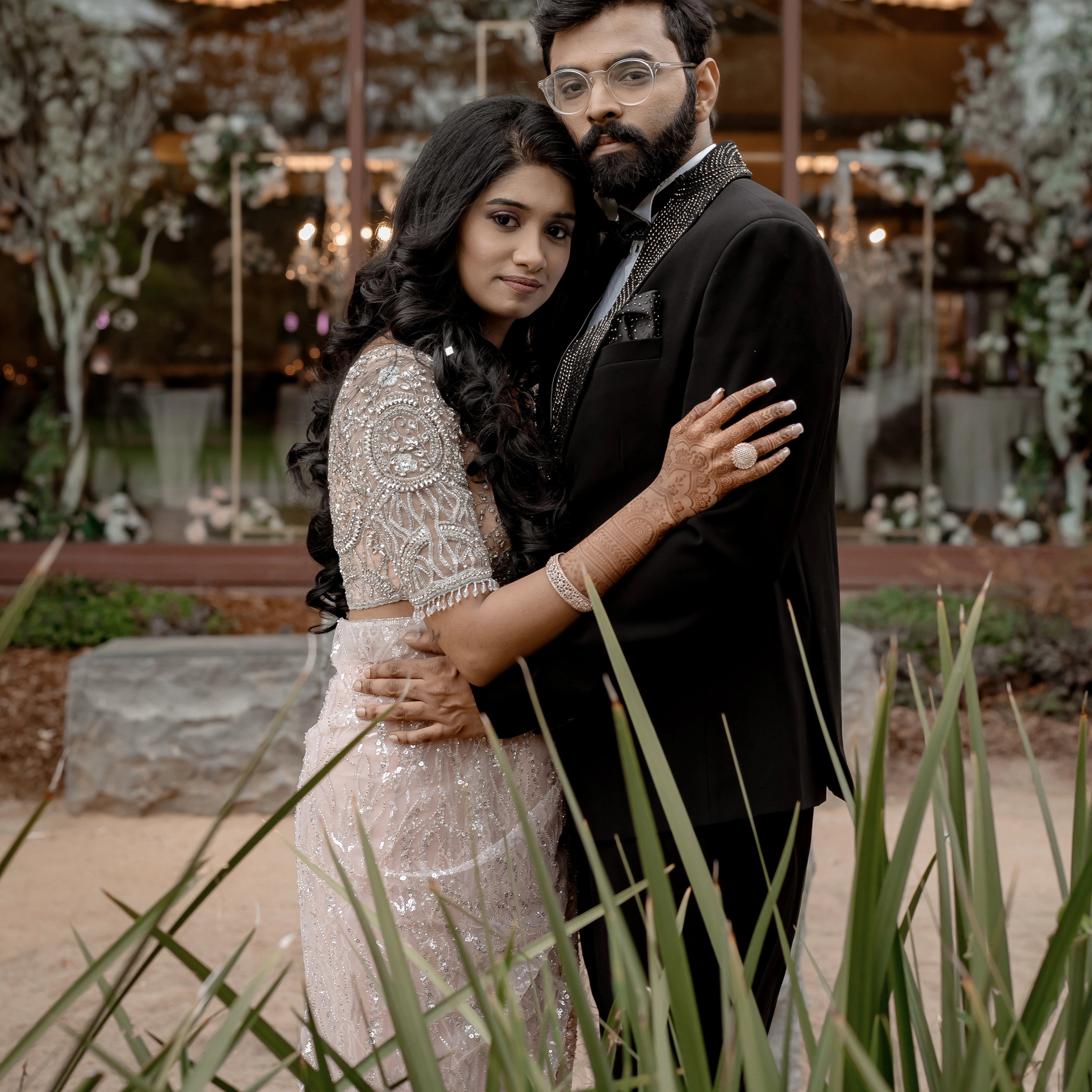 Bride Monica from USA posing with groom for photo in a blush tulle blouse handcrafted by team Archana Karthick.