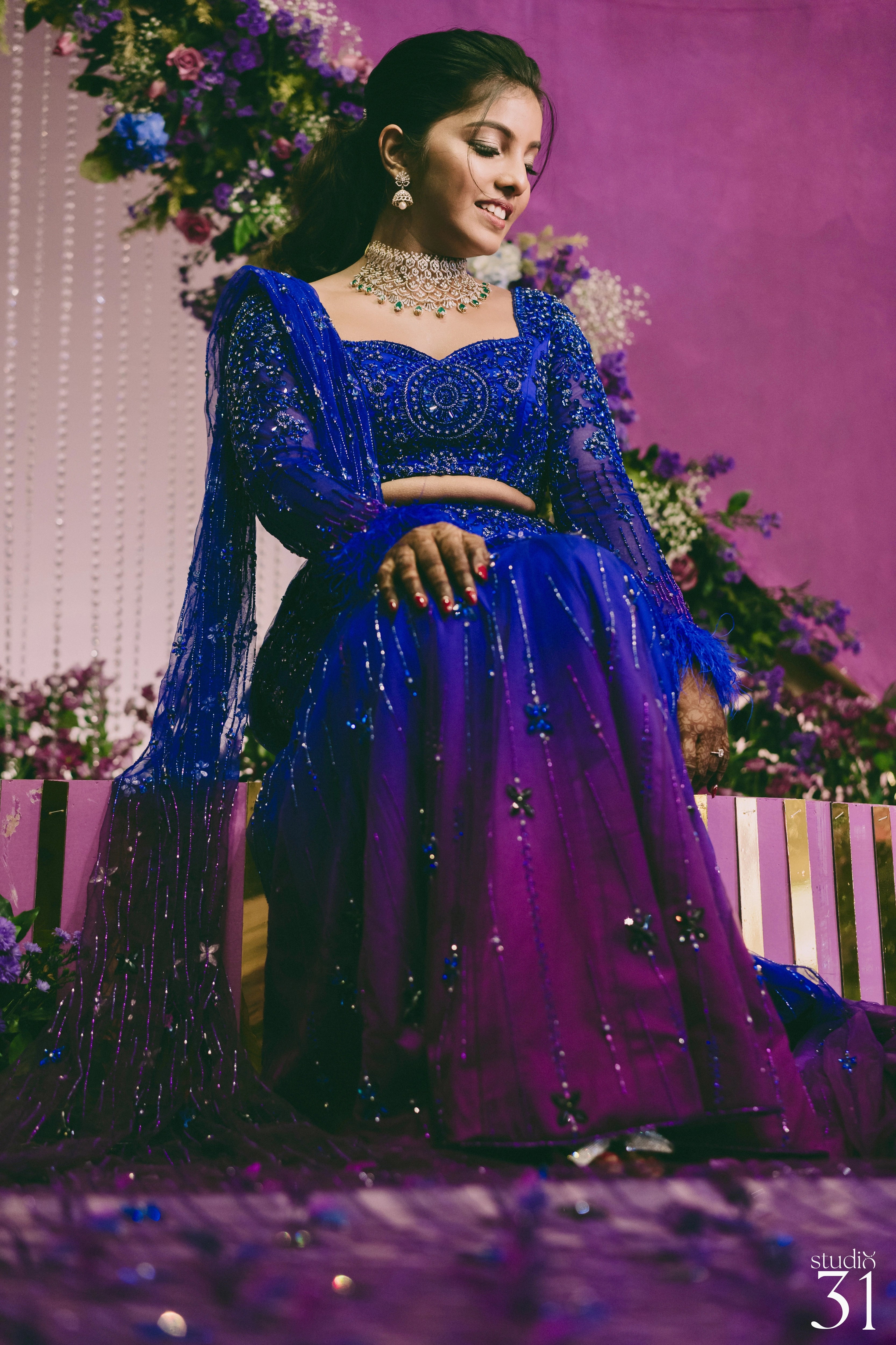 Bride Pooja posing seated in a blue and purple mermaid draped lehenga by team Archana Karthick.