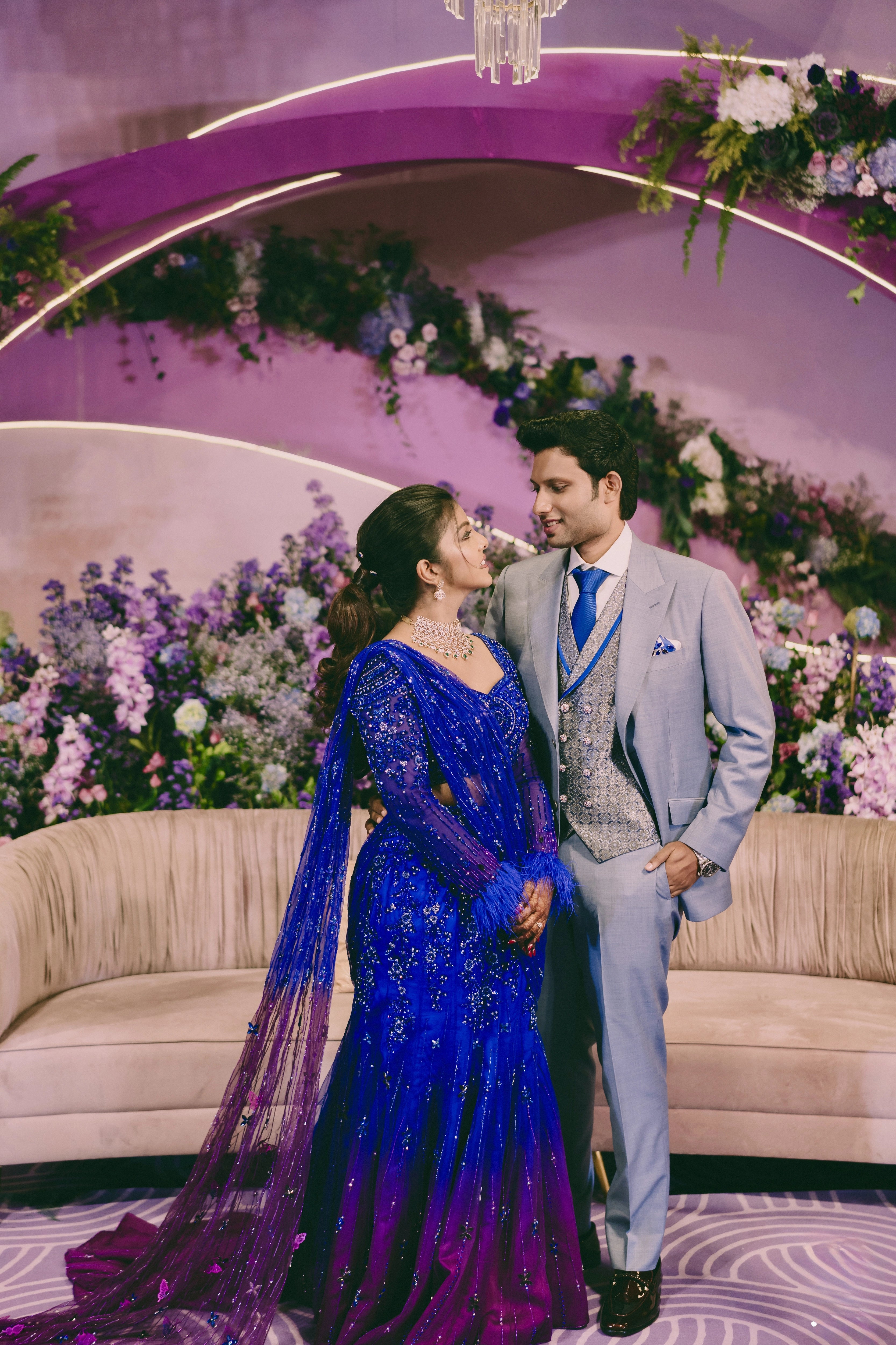 Bride Pooja posing with groom in a blue and purple mermaid draped lehenga by team Archana Karthick.