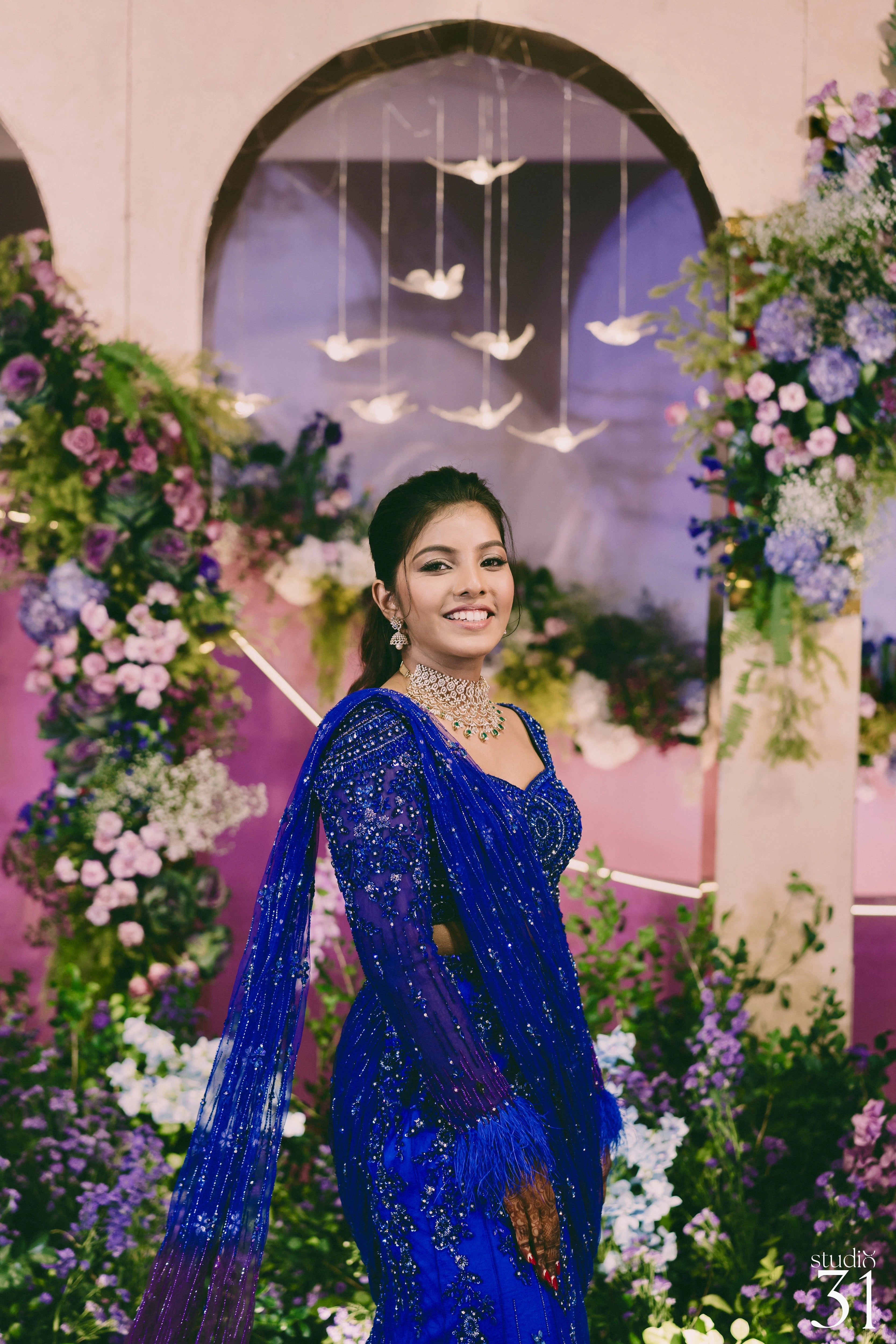 Bride Pooja smiling for photoshoot in a blue and purple mermaid draped lehenga by team Archana Karthick.