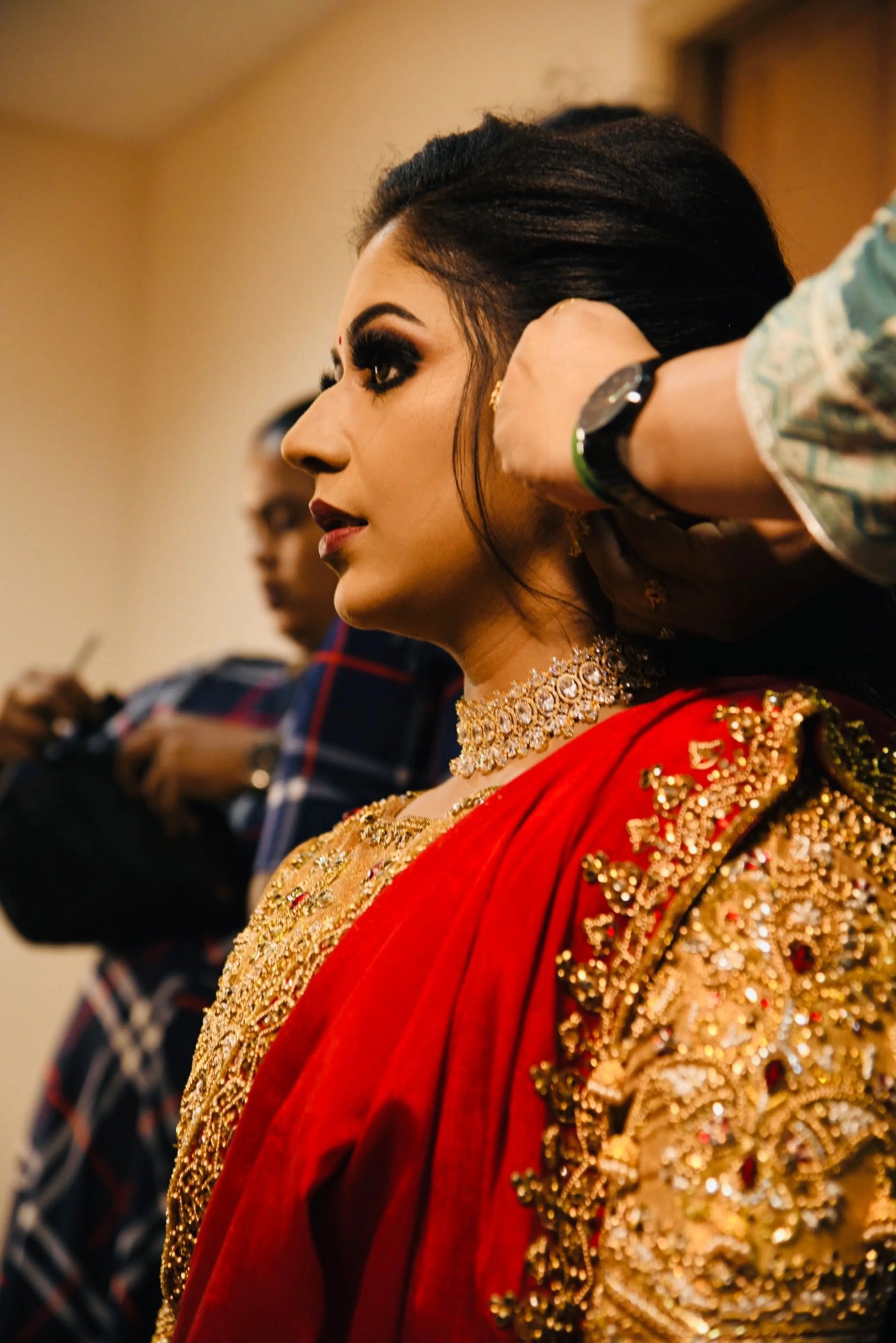 Bride Raji from Ireland in a red and gold silk half saree during makeup, handcrafted intricately with stones, zardozi, beads, sequins and rhinestones by team Archana Karthick