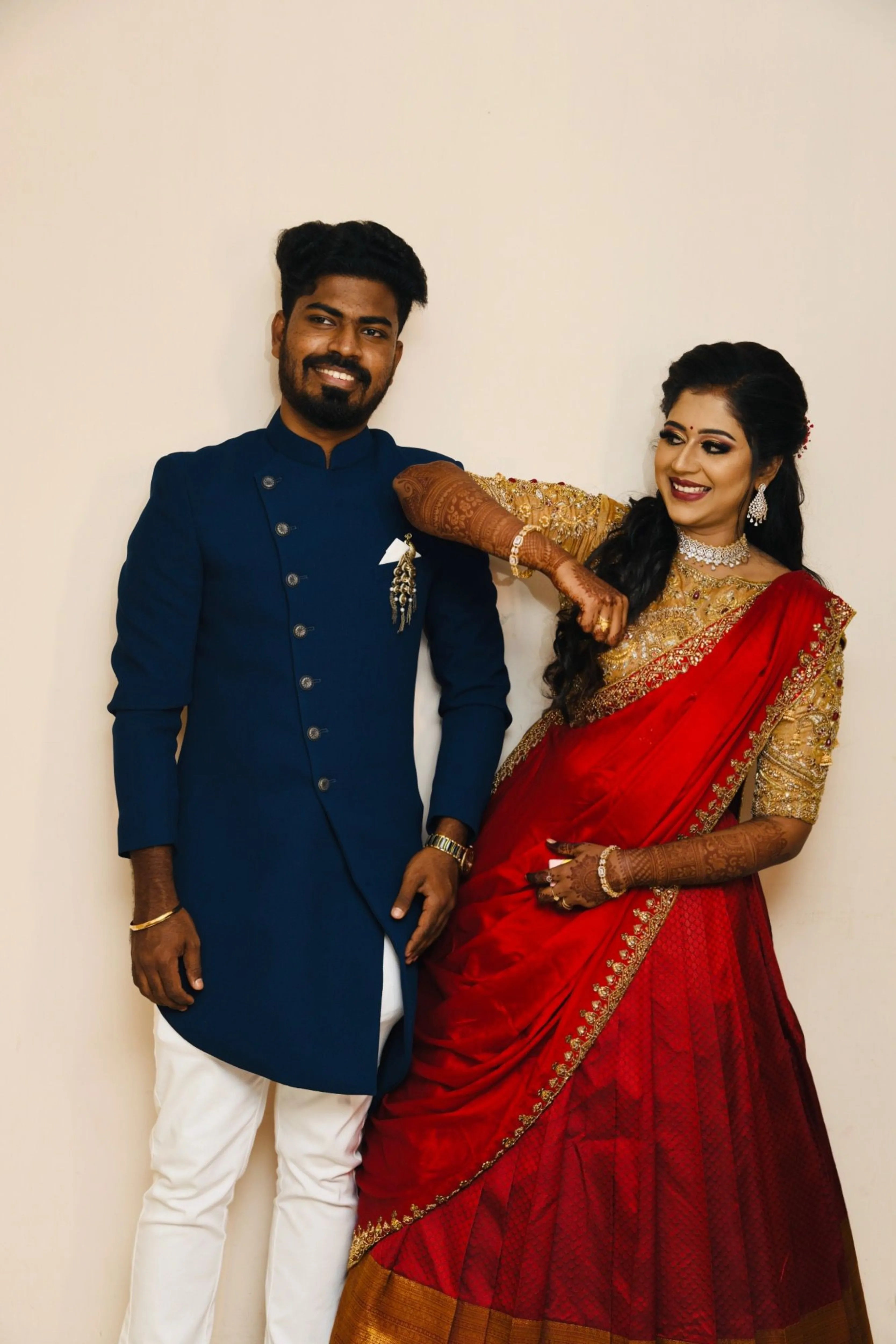 Bride Raji from Ireland smiling with groom in a red and gold silk half saree during makeup, handcrafted intricately with stones, zardozi, beads, sequins and rhinestones by team Archana Karthick