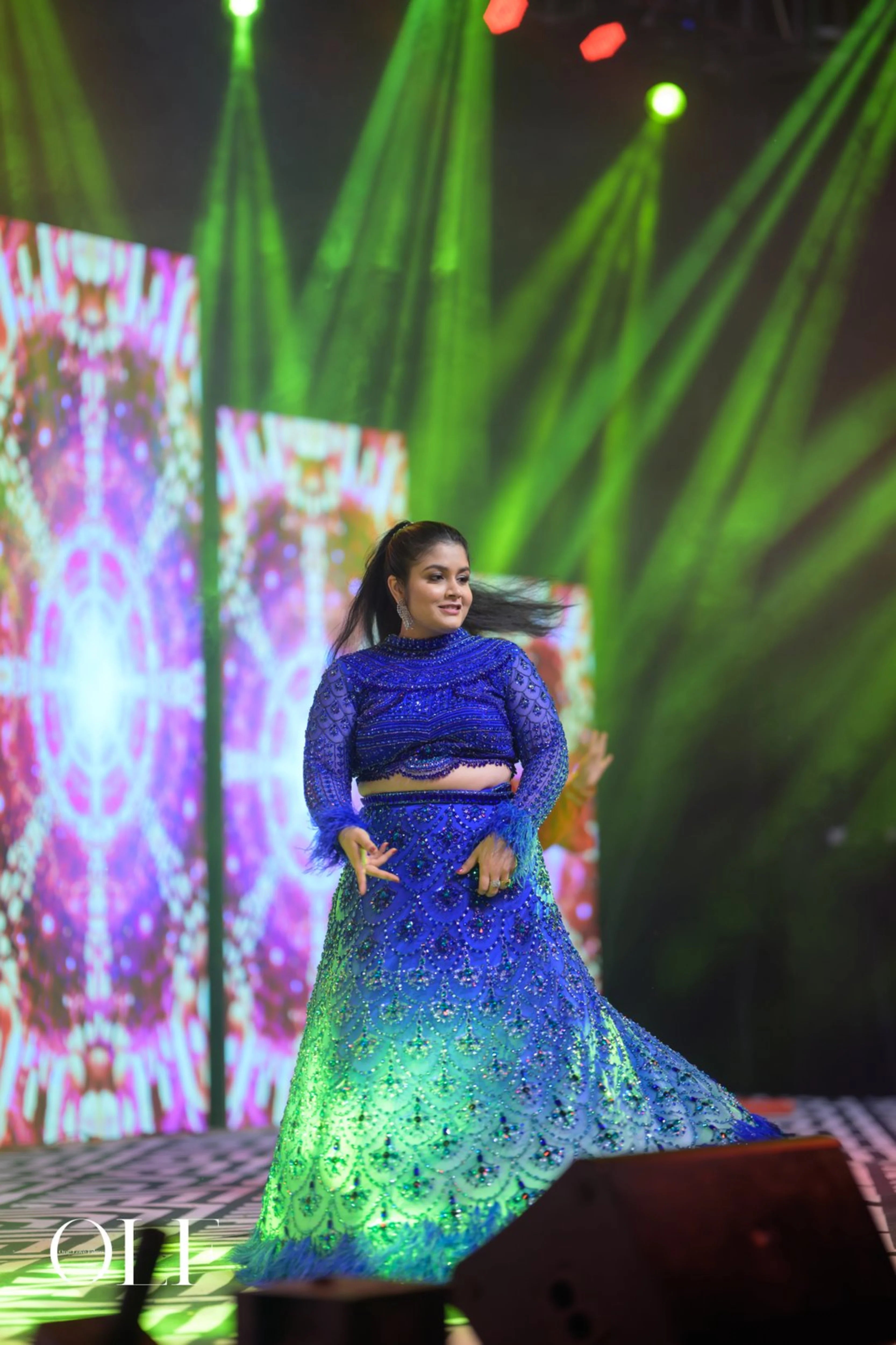 Bride Rasagnya dancing on stage in a peacock themed blue tulle lehenga, handcrafted with rhinestones, crystals, cutdana, sequins and feathers by team Archana Karthick.