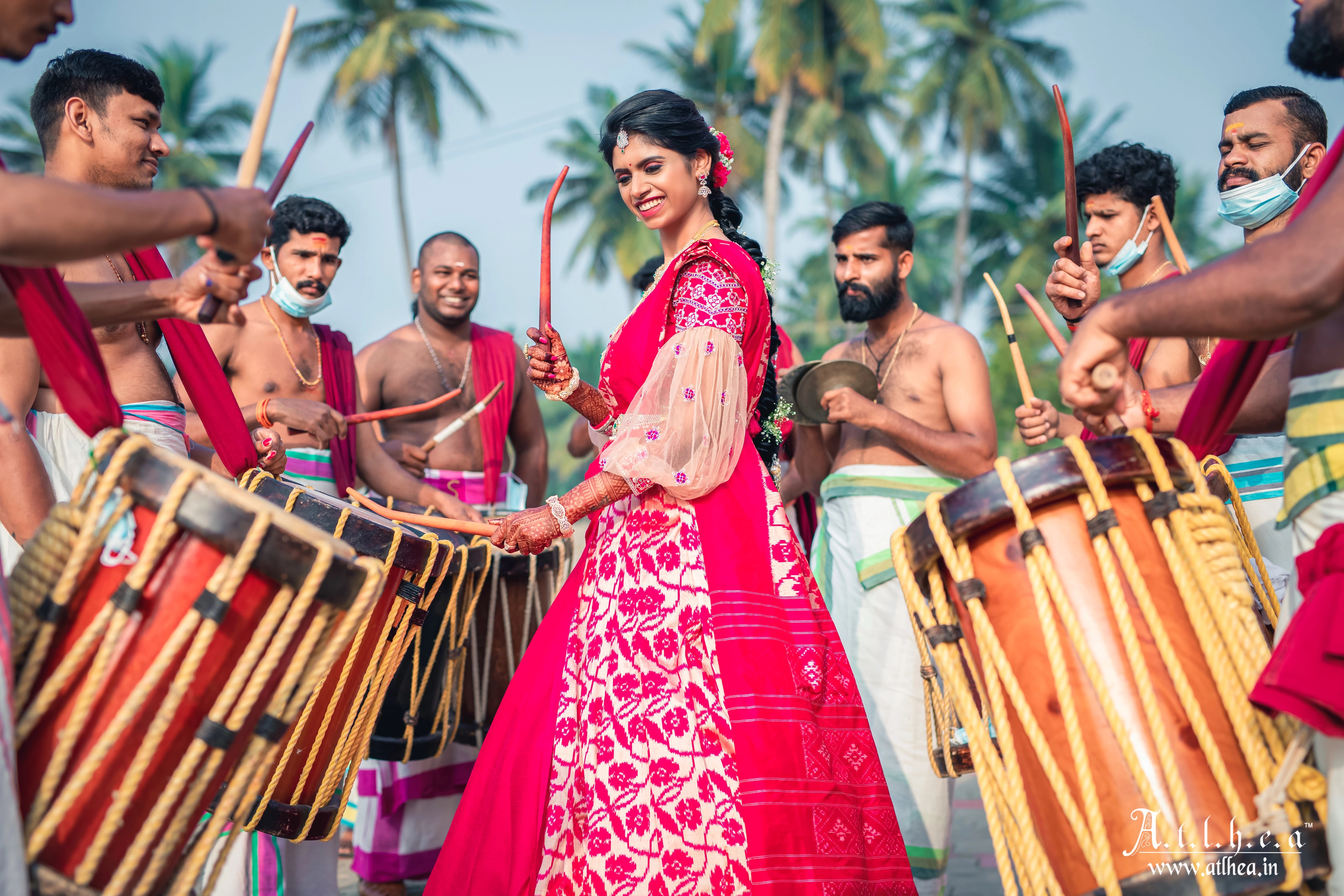 Bride Sahana posing with musicians in a raspberry raw silk half saree, handcrafted intricately with mirror, stones, zardozi and resham by team Archana Karthick.