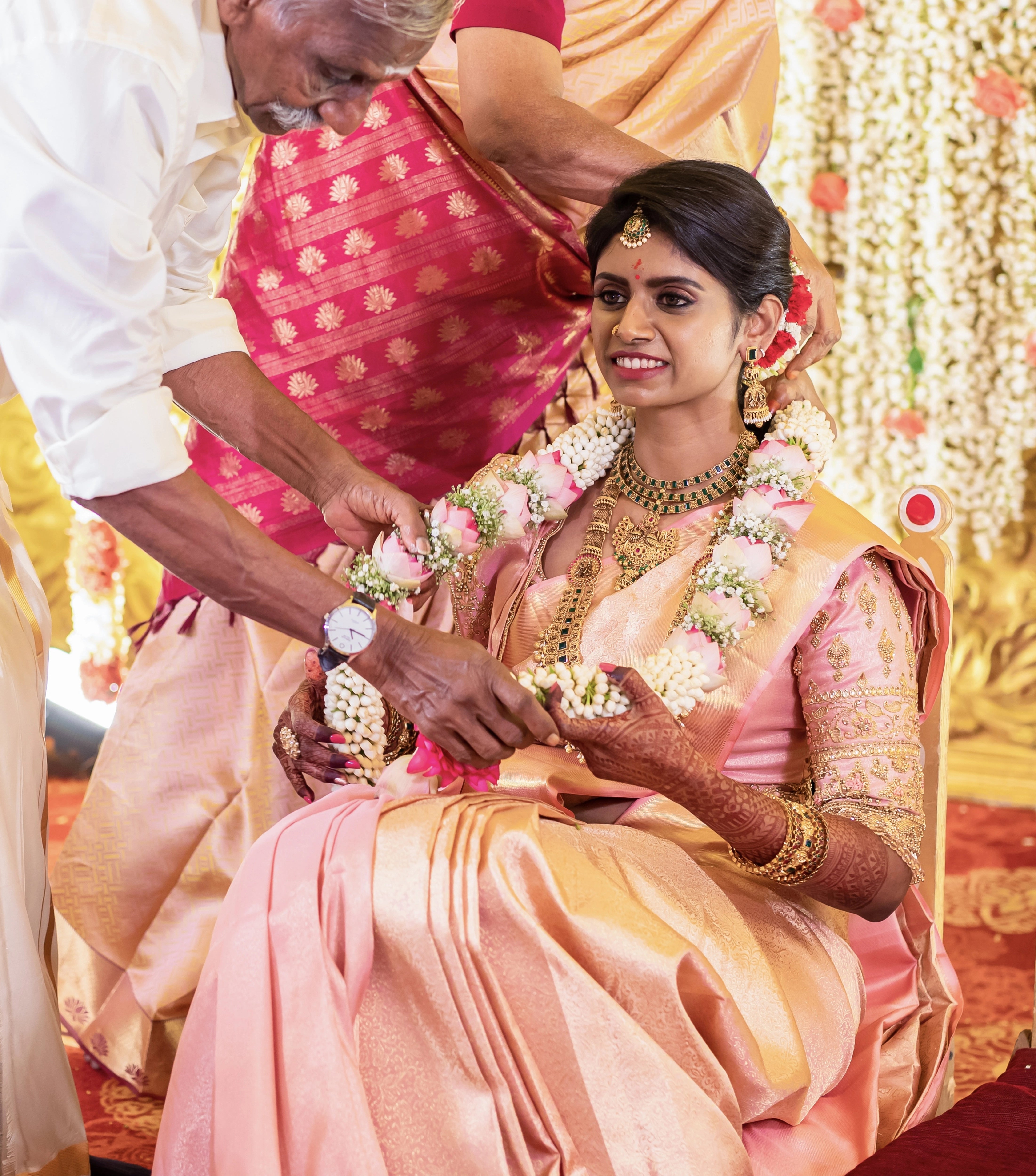 Bride Sahana with garland in a peach cream silk blouse and belt, handcrafted intricately with beads, cutdana, zari, crystals and resham by team Archana Karthick.