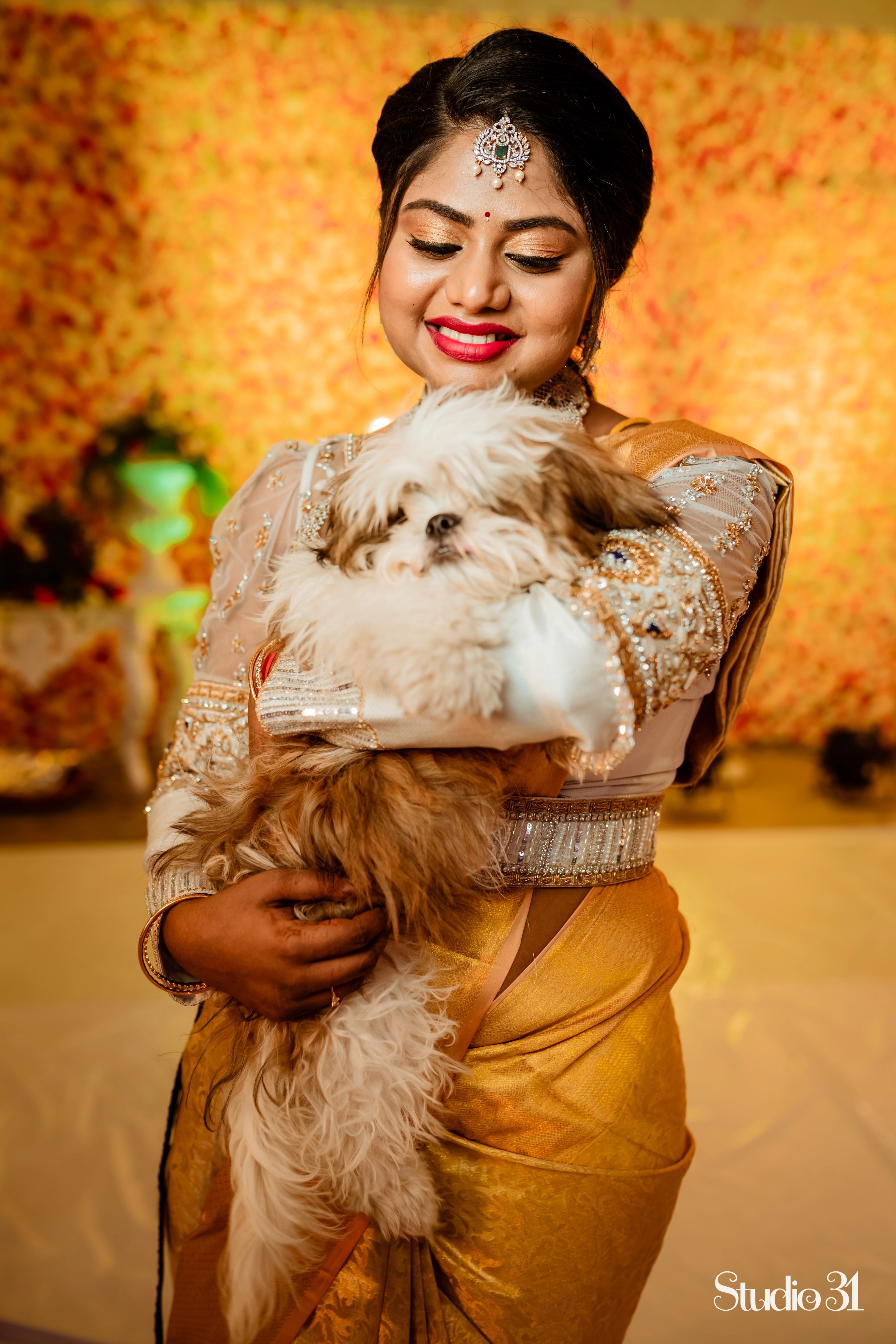 Bride Sailaja from USA smiling with her pet in an ivory tulle and silk blouse and belt, intricately handcrafted by team Archana Karthick.