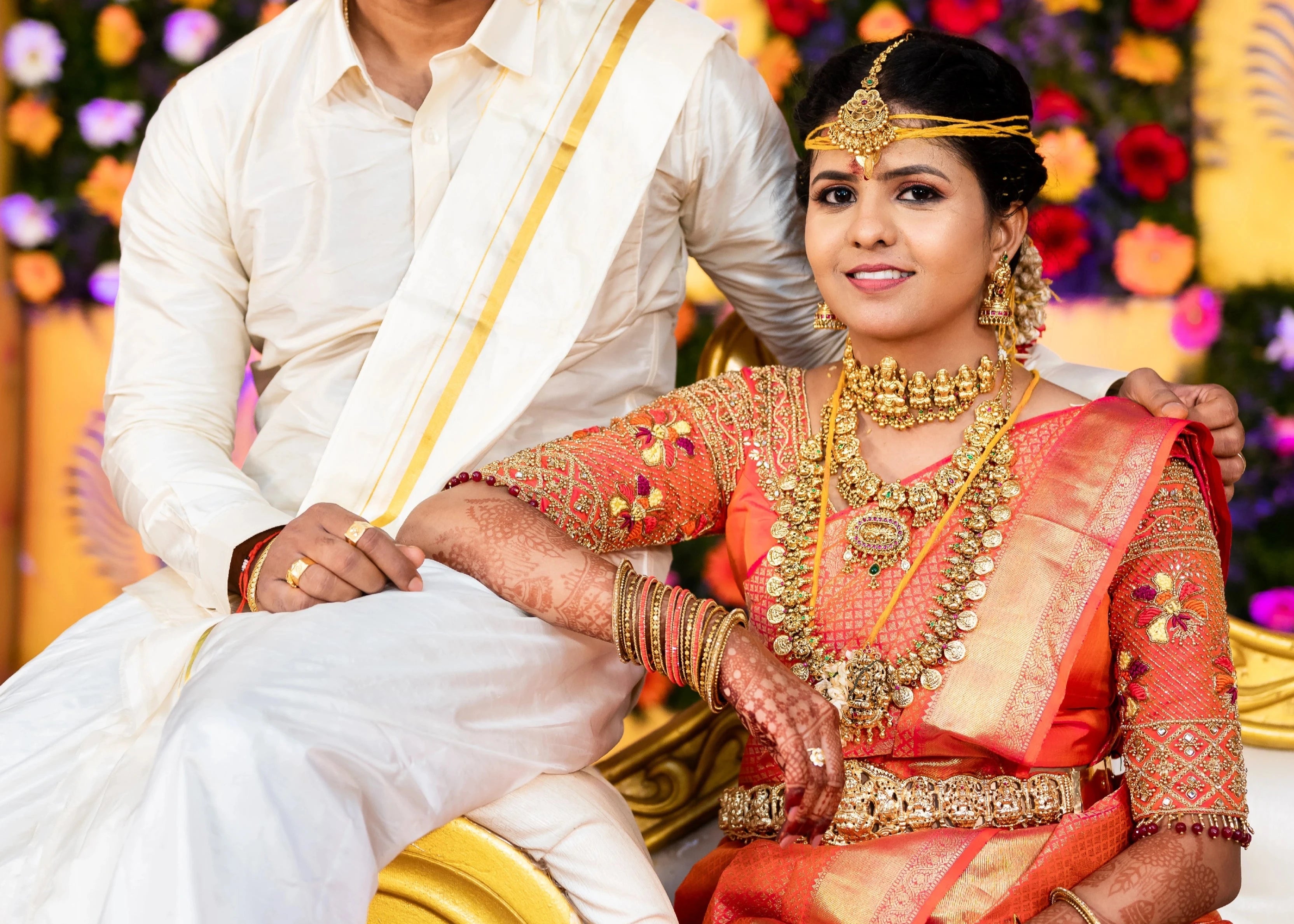 Bride Sarumathi with groom in an orange silk blouse, intricately handcrafted with zardozi, resham, stones and beads by team Archana Karthick.