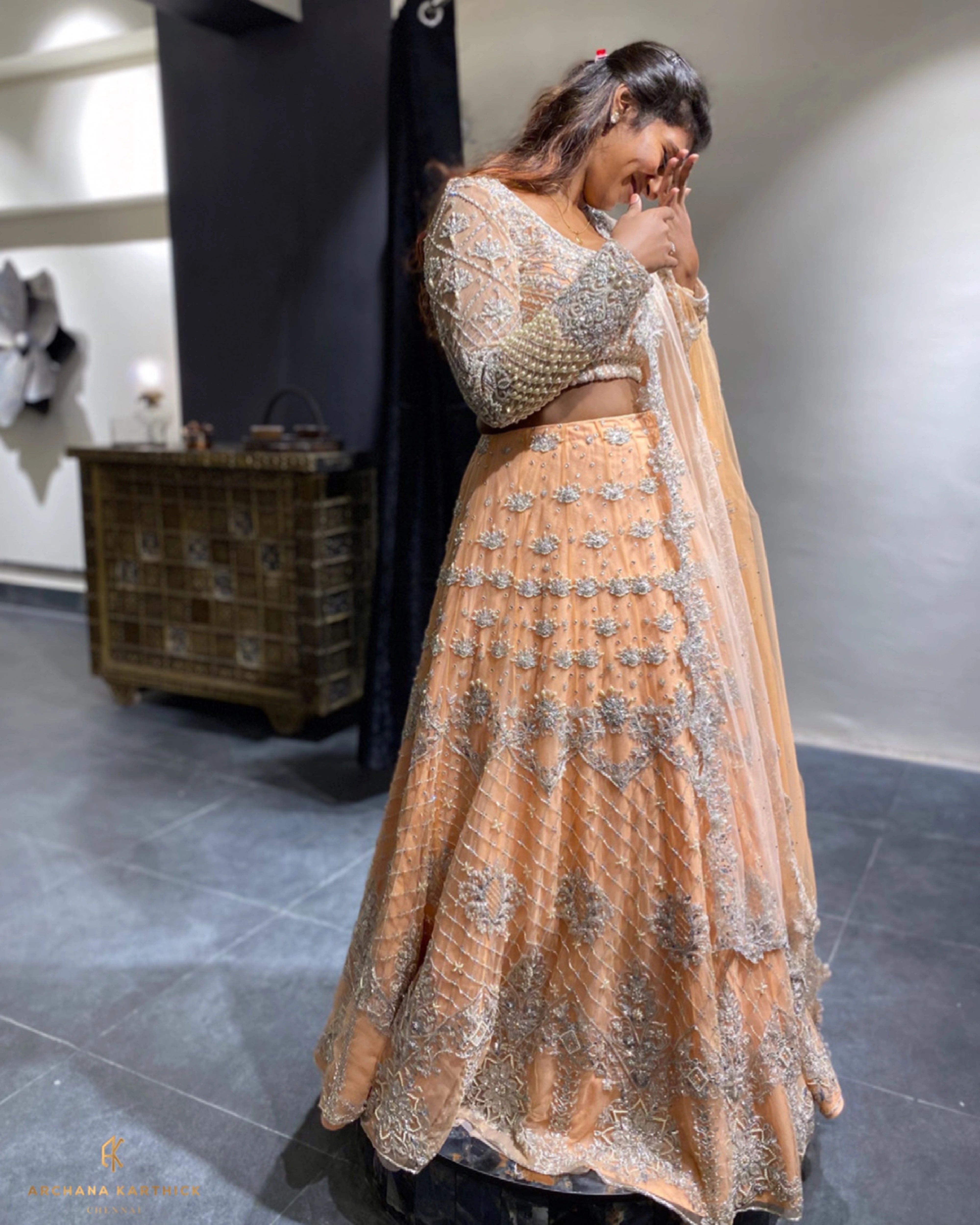 Bride Shanmugapriya posing in a peach tulle reception lehenga, handcrafted by team Archana Karthick.