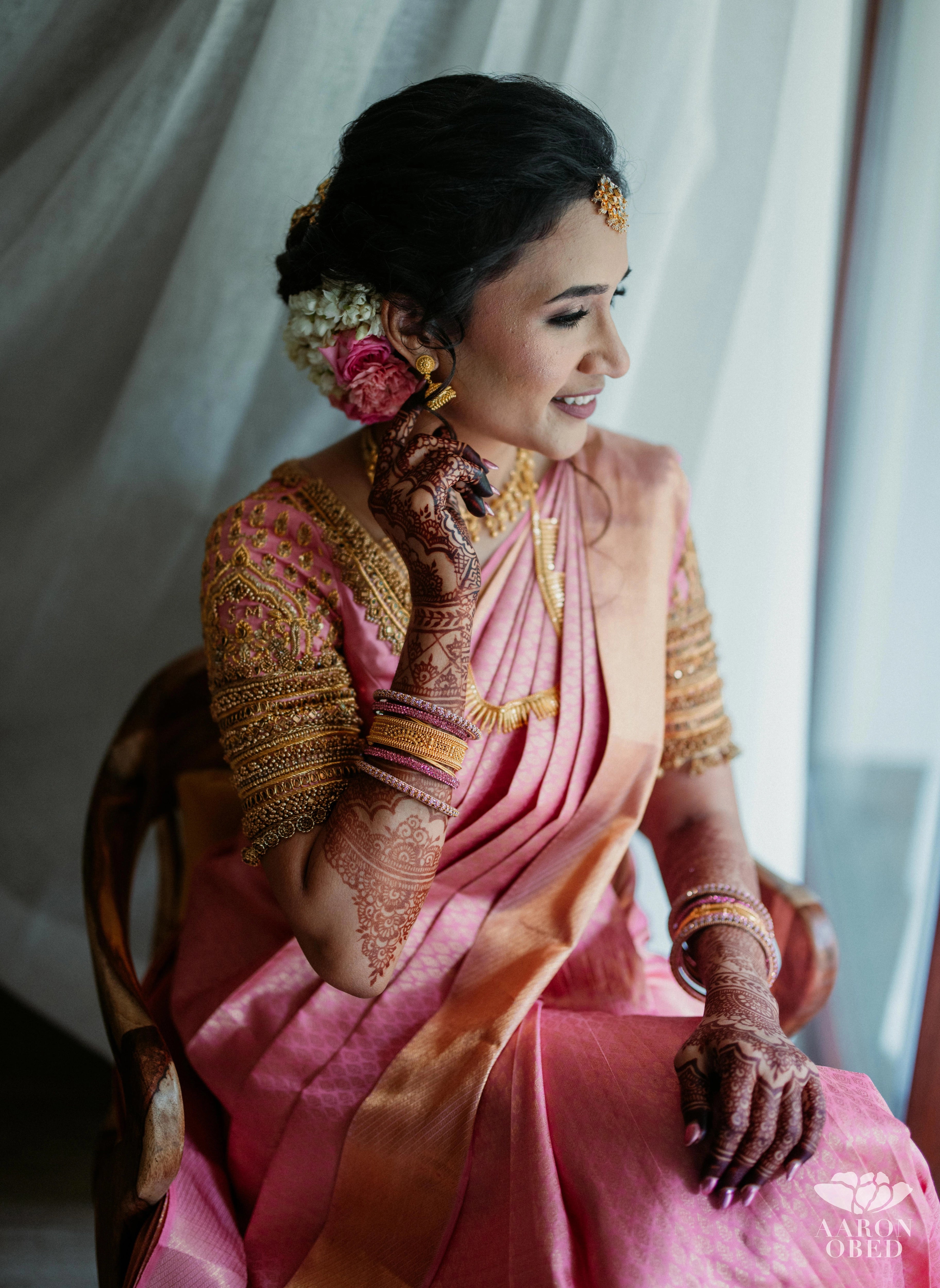 Bride Sharon Jacob during makeup in a pink silk blouse, intricately handcrafted with zardozi, stones, sequins and beads by team Archana Karthick.