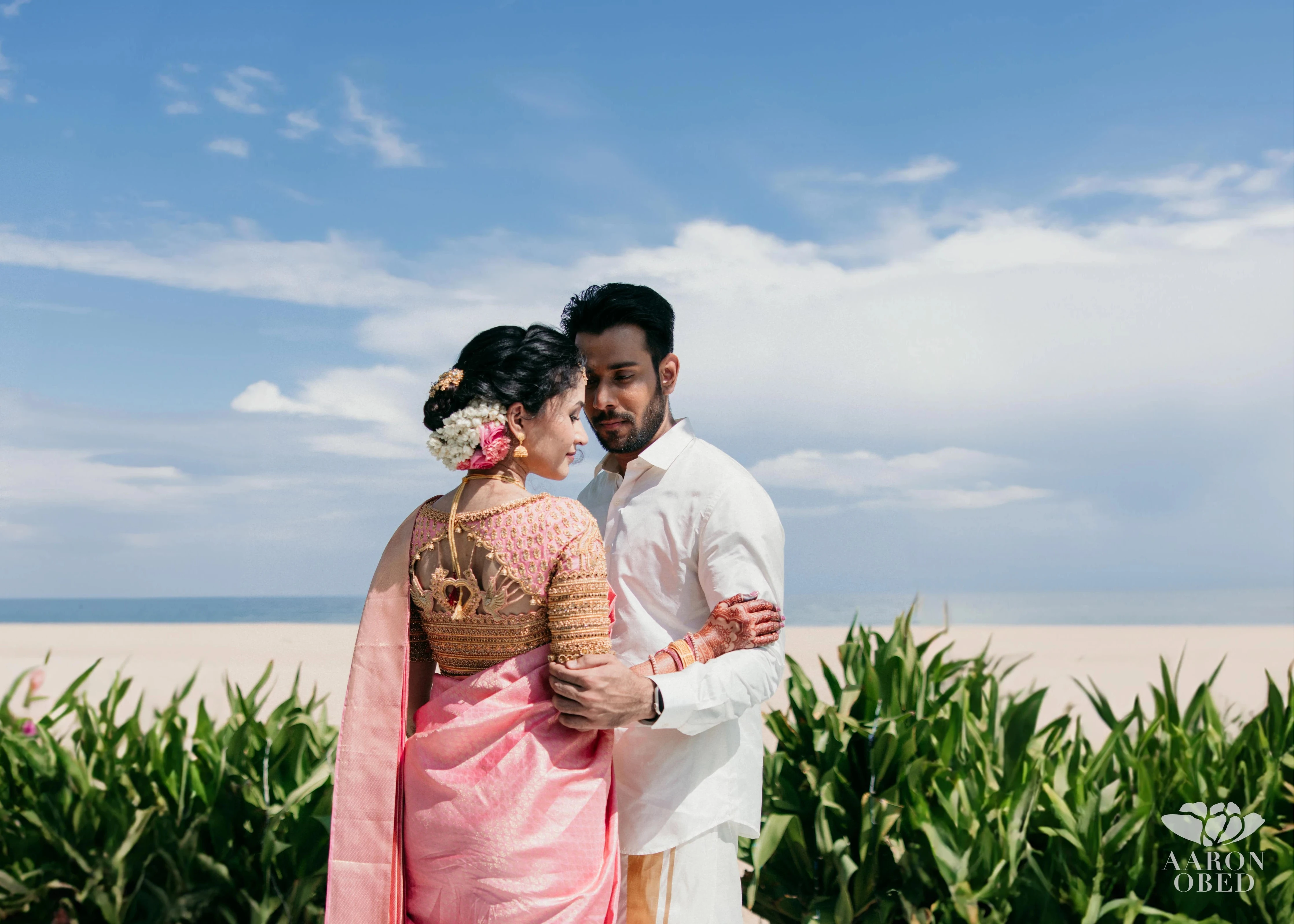 Bride Sharon Jacob posing with groom in a pink silk blouse, intricately handcrafted with zardozi, stones, sequins and beads by team Archana Karthick.