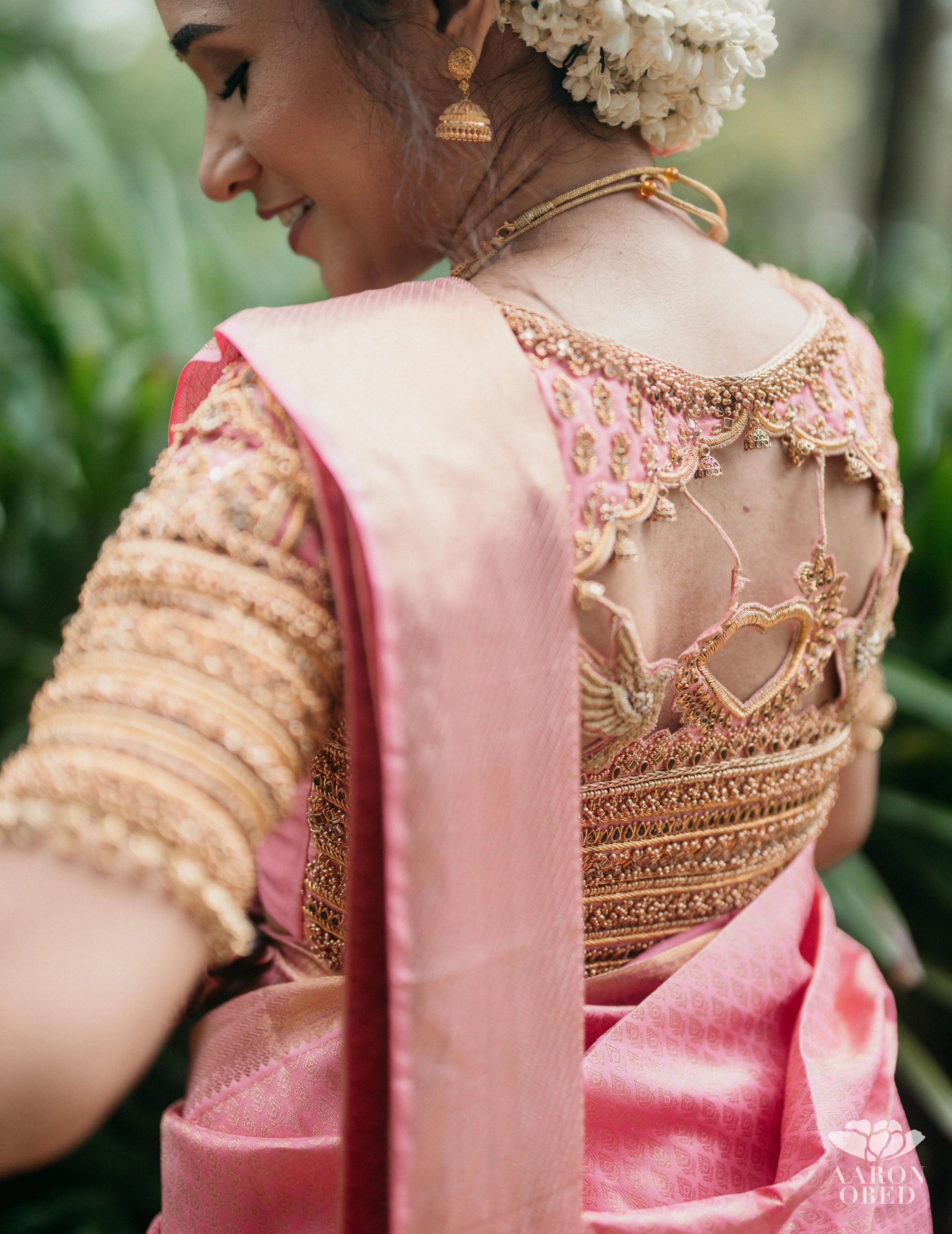 Bride Sharon Jacob showcasing back blouse design in a pink silk blouse, intricately handcrafted with zardozi, stones, sequins and beads by team Archana Karthick.