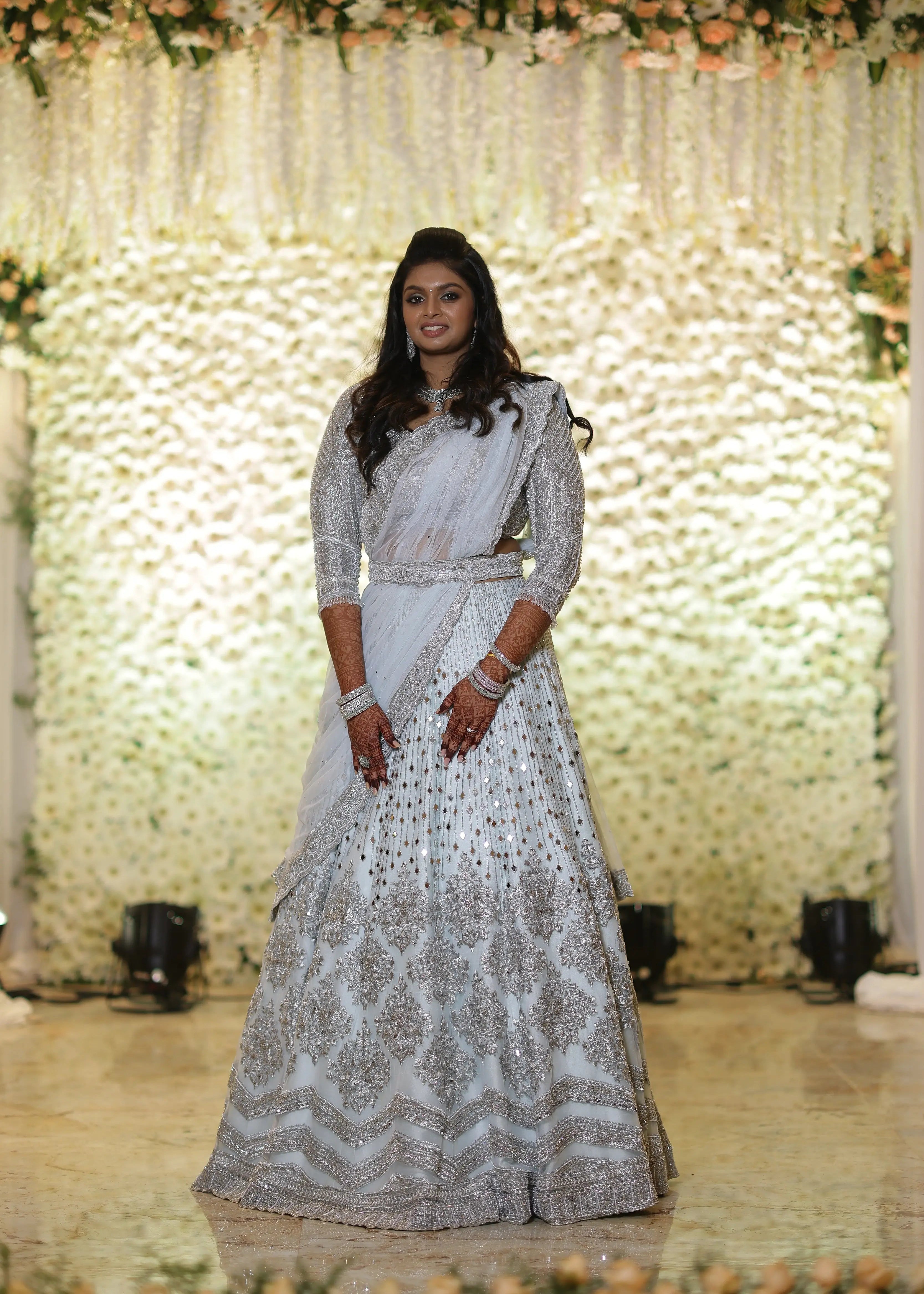 Bride Shreya from USA posing on stage in a handcrafted powder blue net lehenga embellished with mirrors, pearls, zardozi, and crystals.