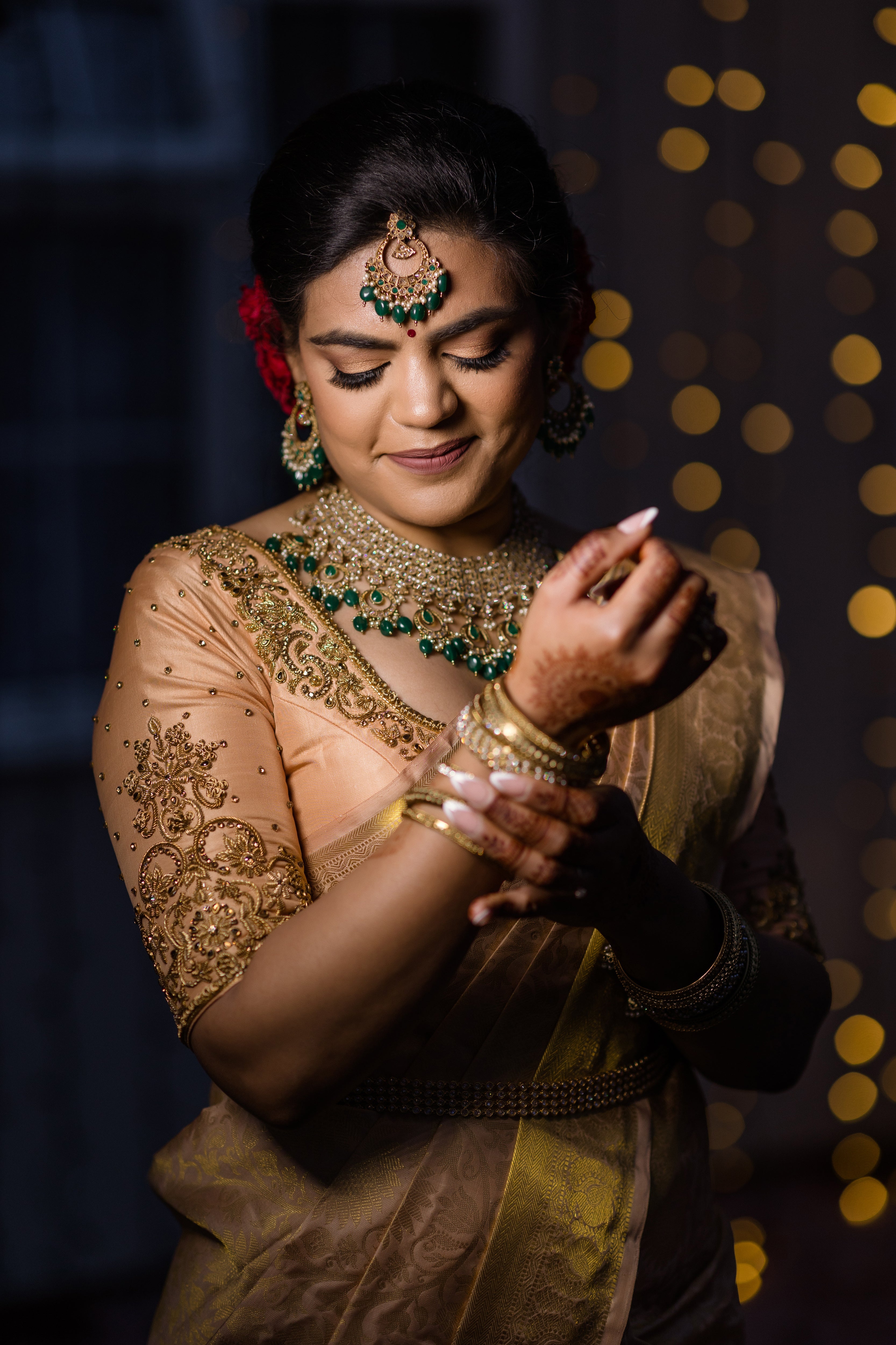Bride Sinthuja from Middlesex, UK in a handcrafted silk blouse designed by Archana Karthick. Looking down shyly adjusting her gold bangles.