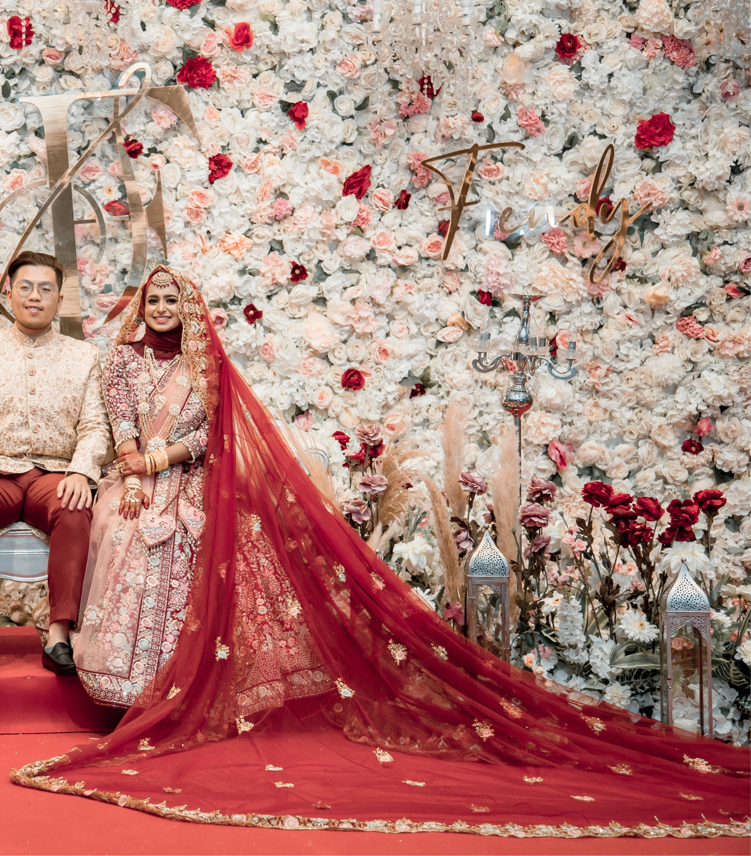 Bride Syaza from Malaysia posing on stage in a maroon tulle veil, intricately handcrafted with zardozi, beads, sequins, stones and resham by team Archana Karthick.