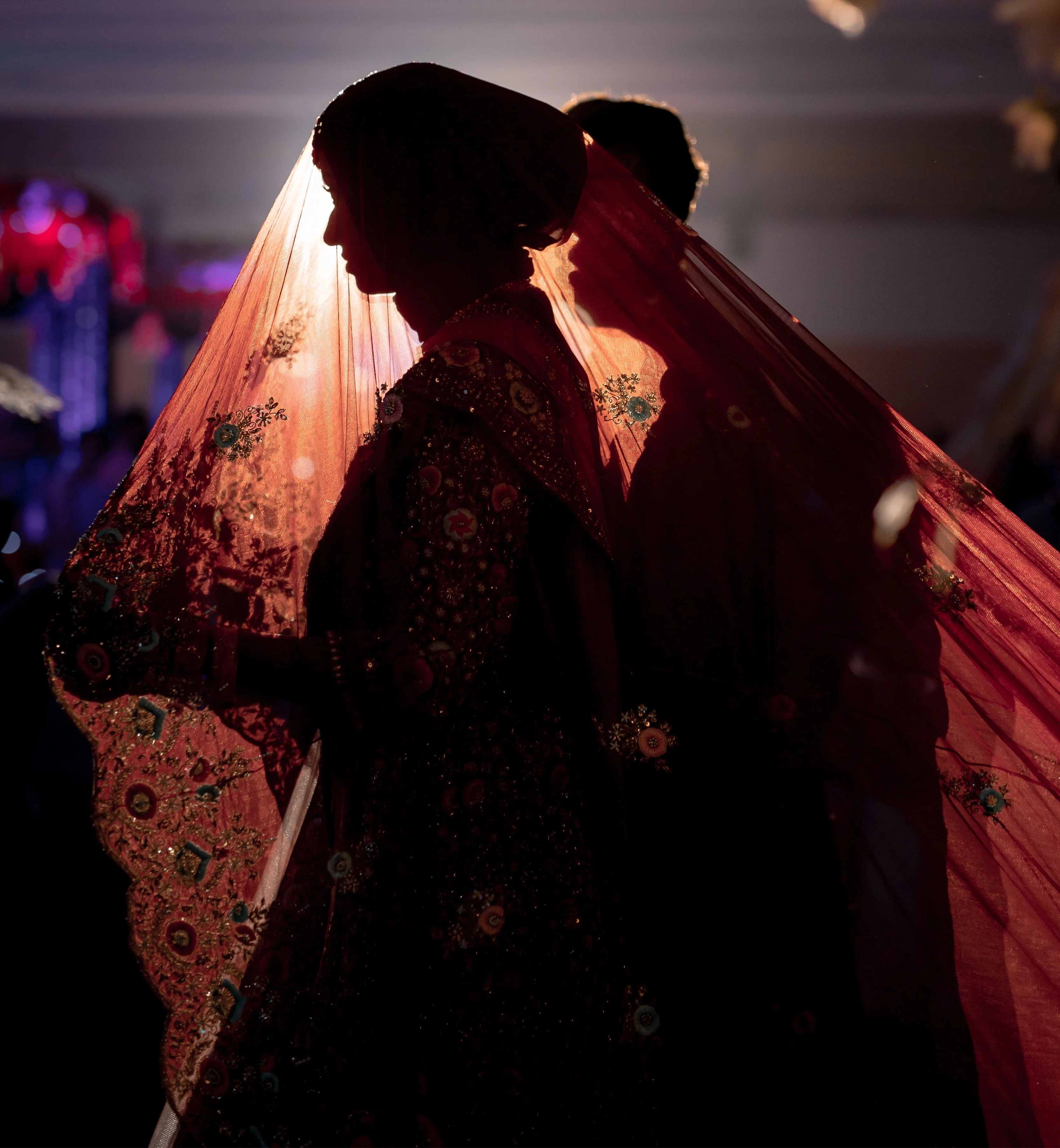 Bride Syaza from Malaysia posing on stage with groom in a maroon tulle veil, intricately handcrafted with zardozi, beads, sequins, stones and resham by team Archana Karthick.