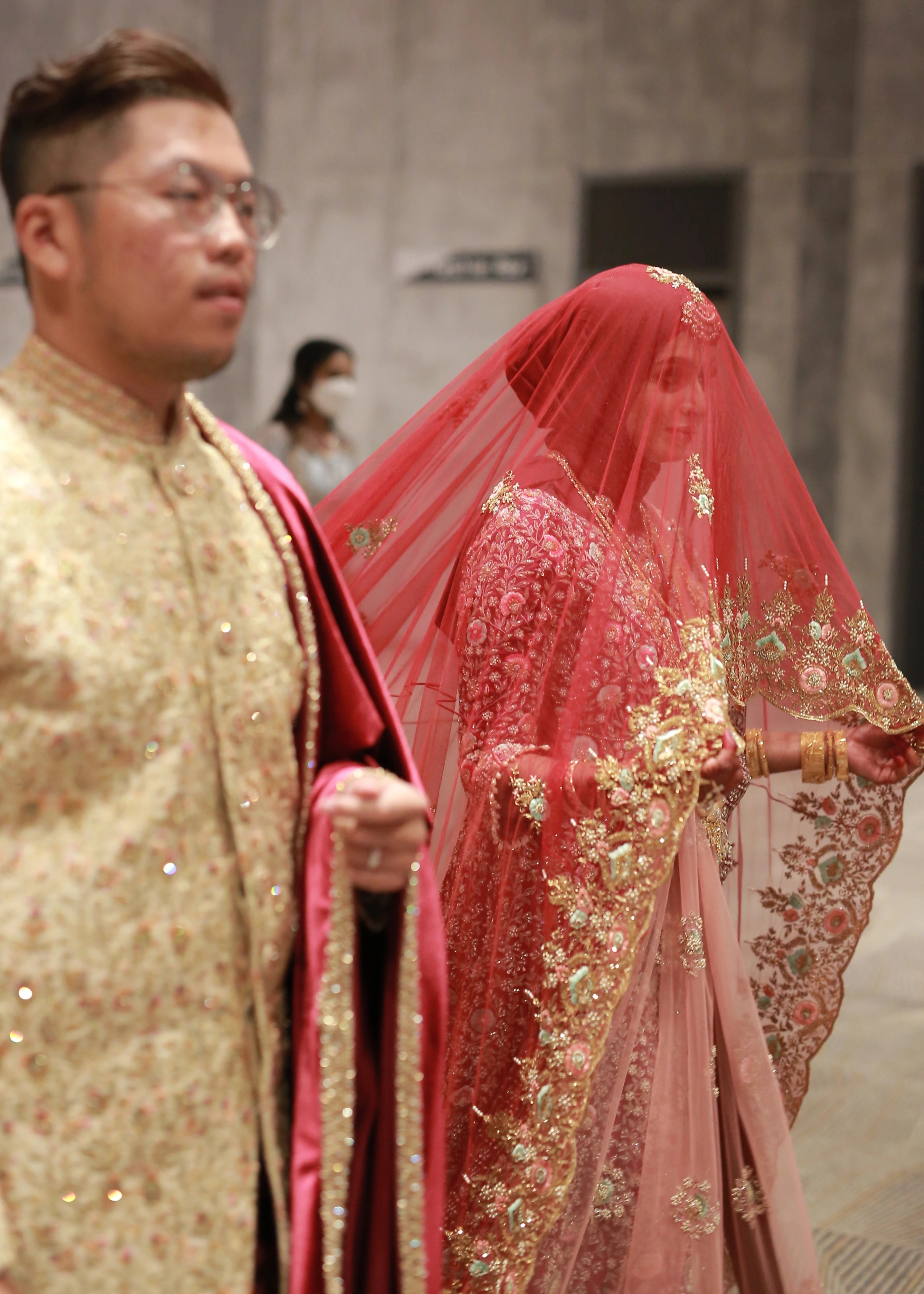 Bride Syaza from Malaysia posing with groom in a maroon tulle veil, intricately handcrafted with zardozi, beads, sequins, stones and resham by team Archana Karthick.