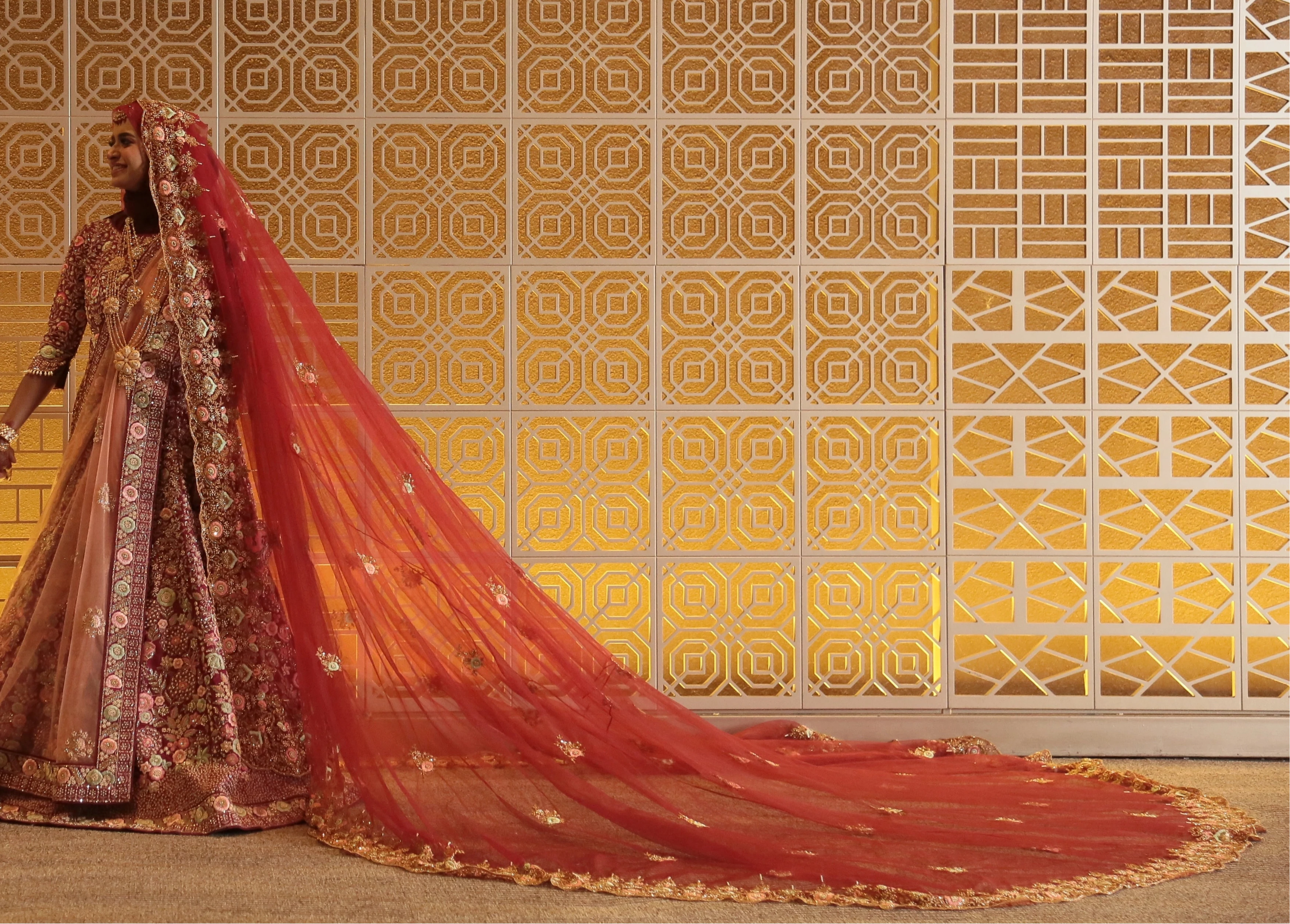 Bride Syaza from Malaysia smiling with groom in a maroon tulle veil, intricately handcrafted with zardozi, beads, sequins, stones and resham by team Archana Karthick.