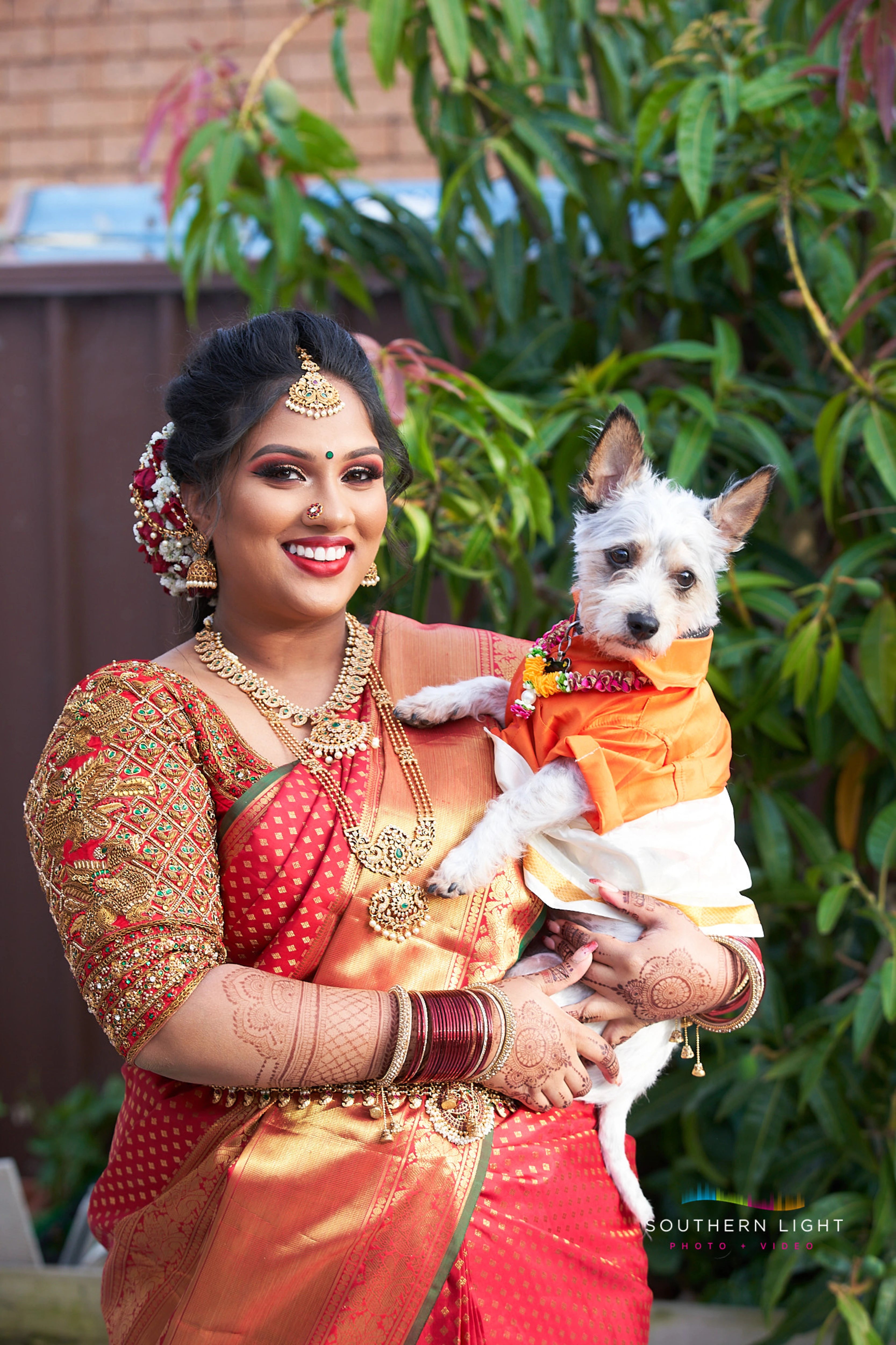 Bride Thena from Australia smiling with her pup in a red silk blouse by Archana Karthick