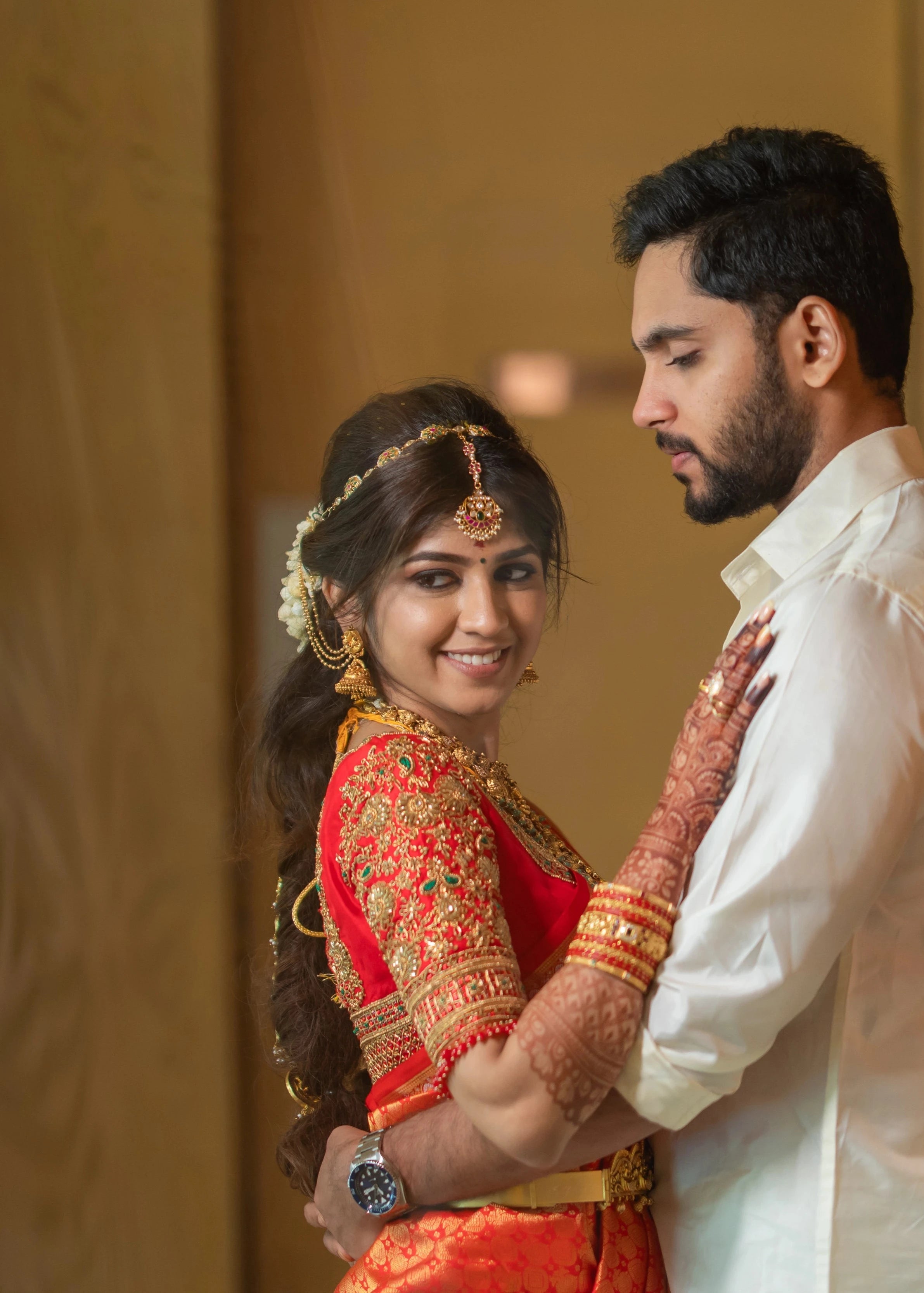 Bride Vaishali Dheenan posing with groom in a red silk blouse for her muhurtham, handcrafted with zardozi, sequins, kundan, crystals, beads and resham by team Archana Karthick.