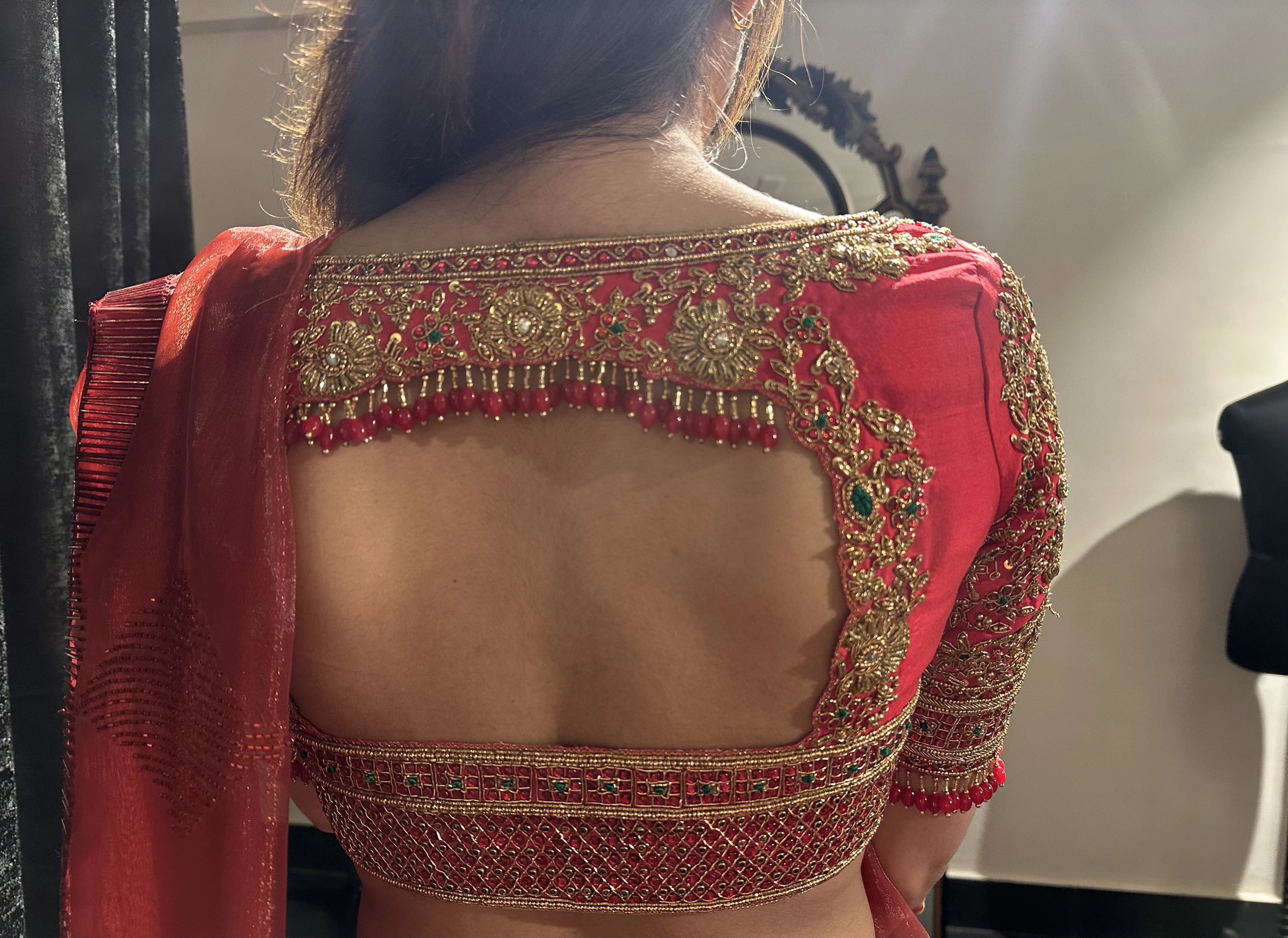 Bride Vaishali Dheenan showcasing back blouse design in a red silk blouse for her muhurtham, handcrafted with zardozi, sequins, kundan, crystals, beads and resham by team Archana Karthick.