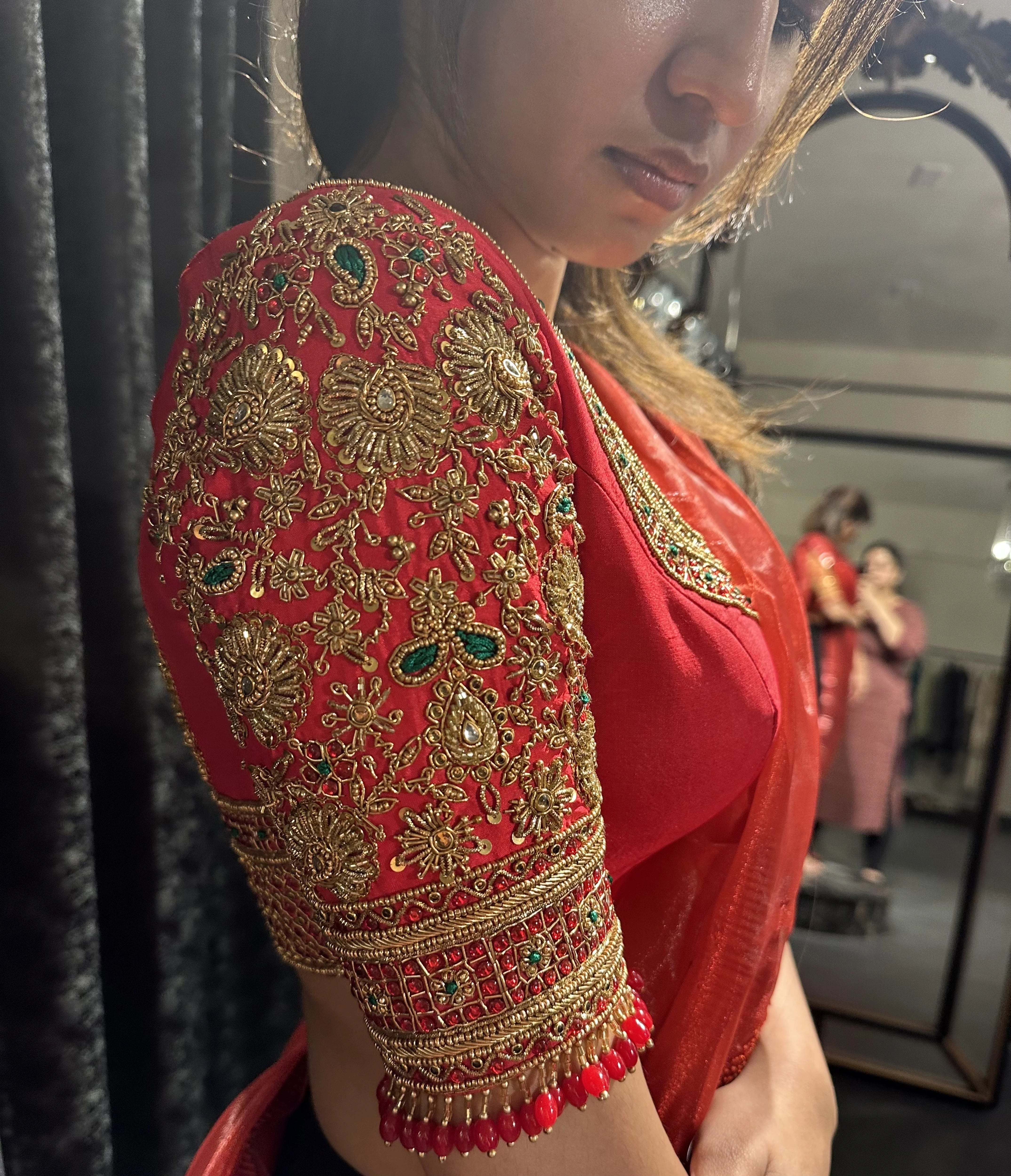 Bride Vaishali Dheenan showcasing sleeve in a red silk blouse for her muhurtham, handcrafted with zardozi, sequins, kundan, crystals, beads and resham by team Archana Karthick.