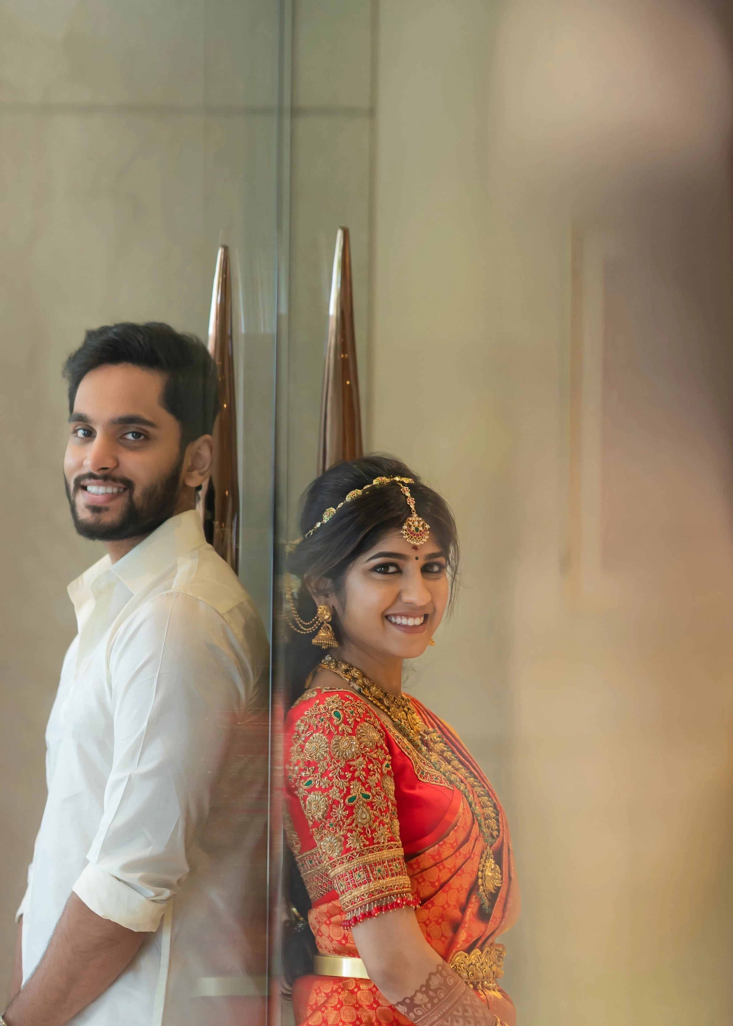 Bride Vaishali Dheenan smiling for side profile in a red silk blouse for her muhurtham, handcrafted with zardozi, sequins, kundan, crystals, beads and resham by team Archana Karthick.