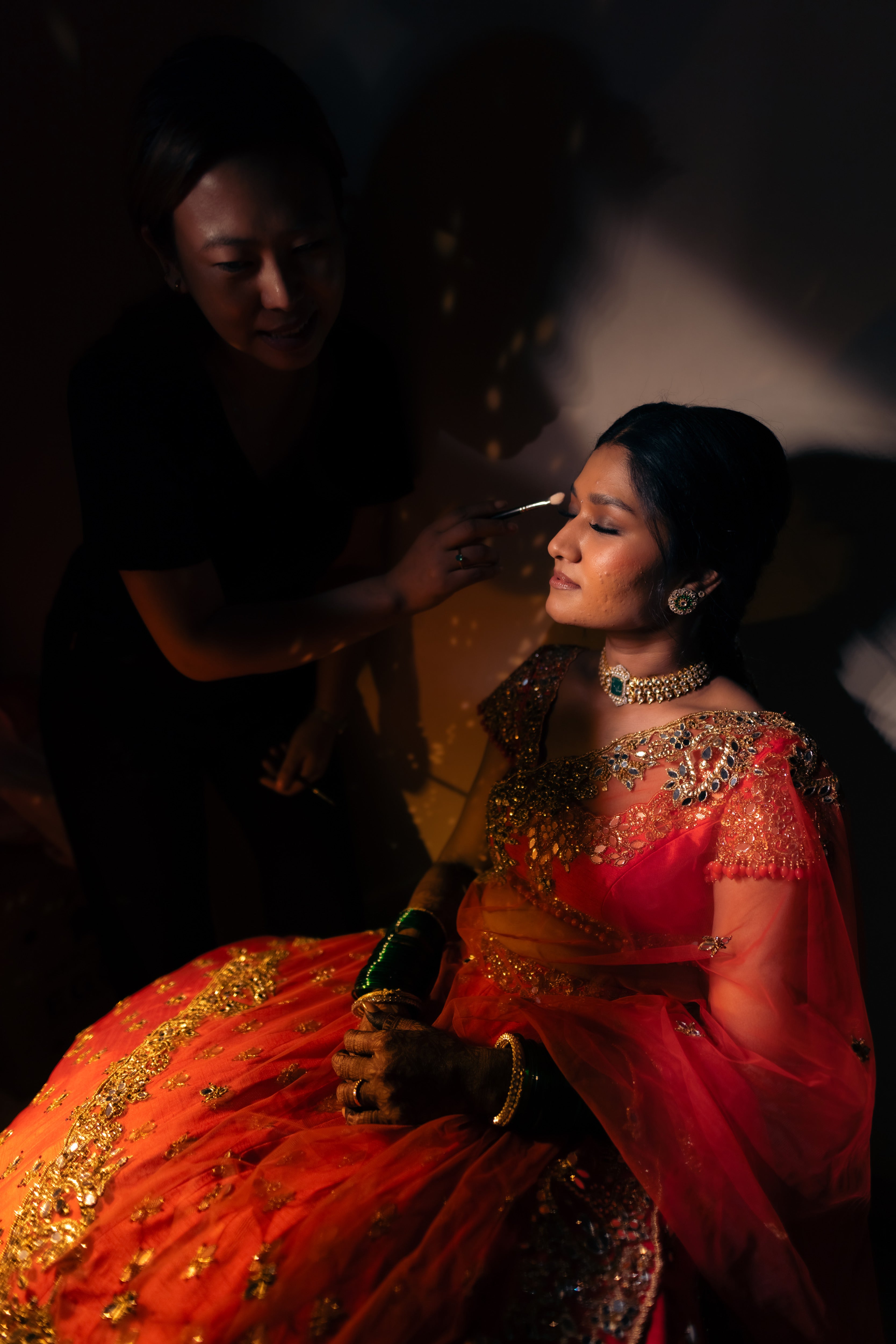 Bride Vaishali from Dubai, in a stunning mirror and zardozi worked orange lehenga designed by Archana Karthick. Here the makeup artist is seen working on the bride.