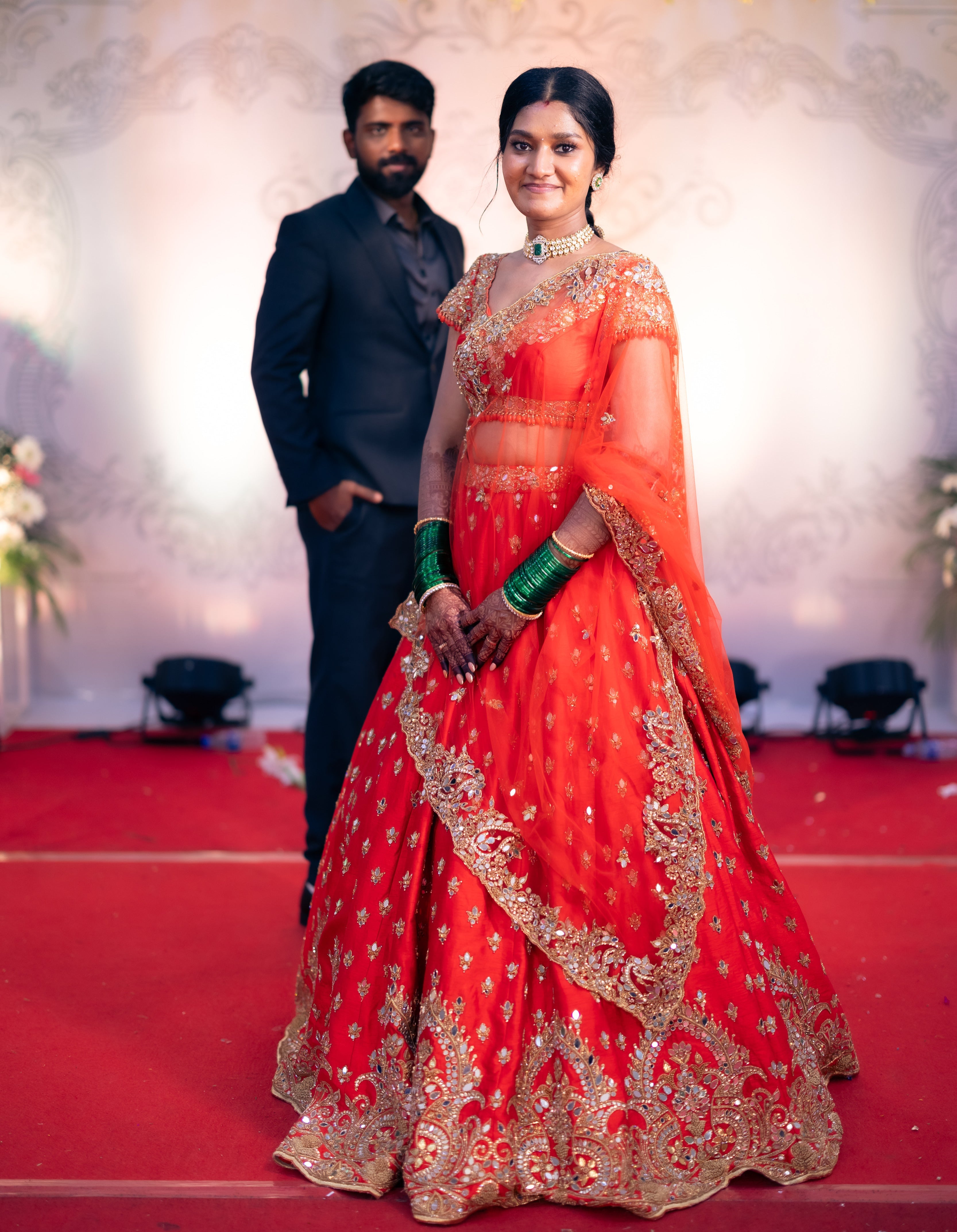 Bride Vaishali from Dubai, in a stunning mirror and zardozi worked orange lehenga designed by Archana Karthick. Here the bride is in front of the groom on the stage.