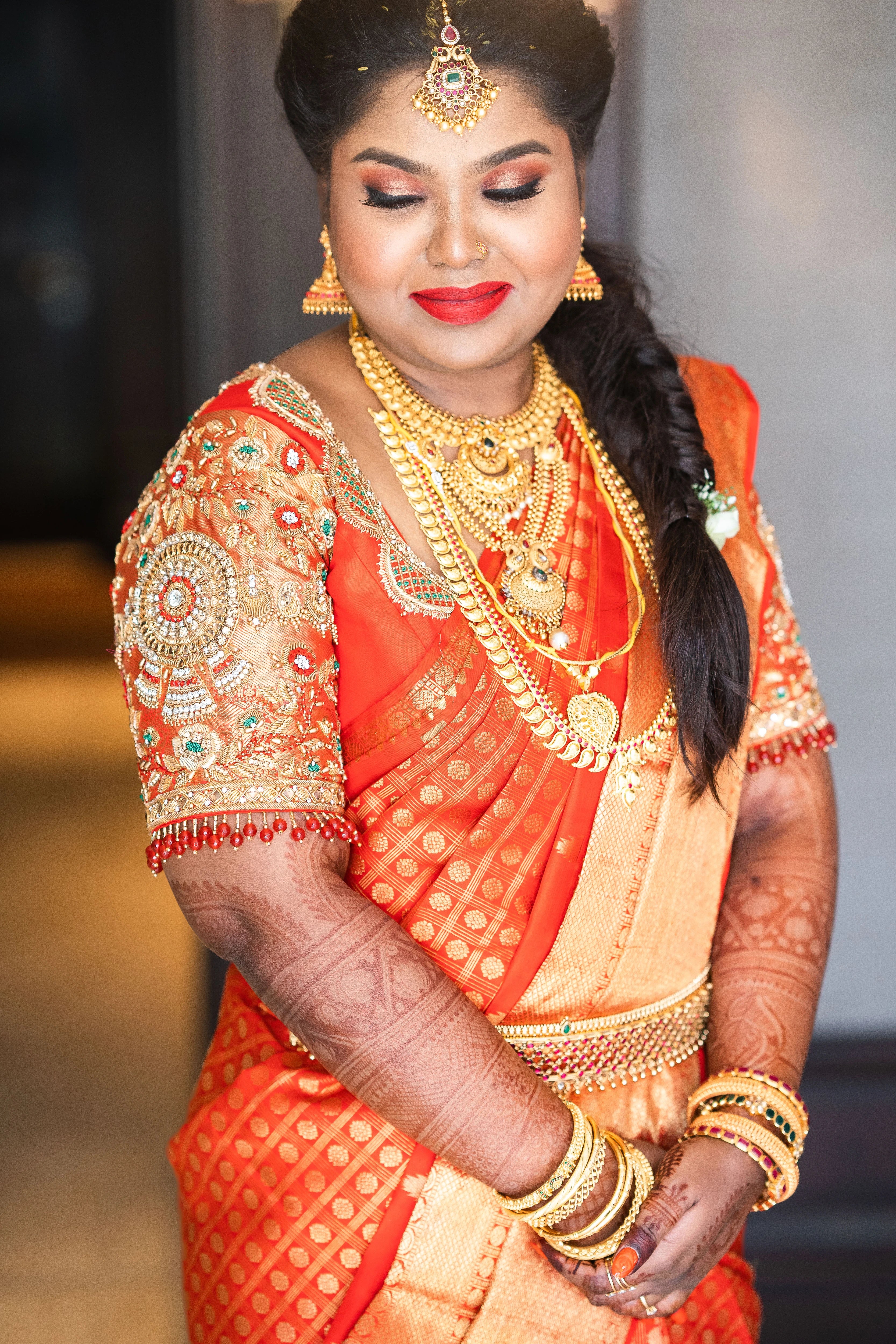 Bride Vanmathi from Chennai smiling in a red and gold silk blouse for her wedding, handcrafted with zardozi, stones, kundan, beads and resham by team Archana Karthick.
