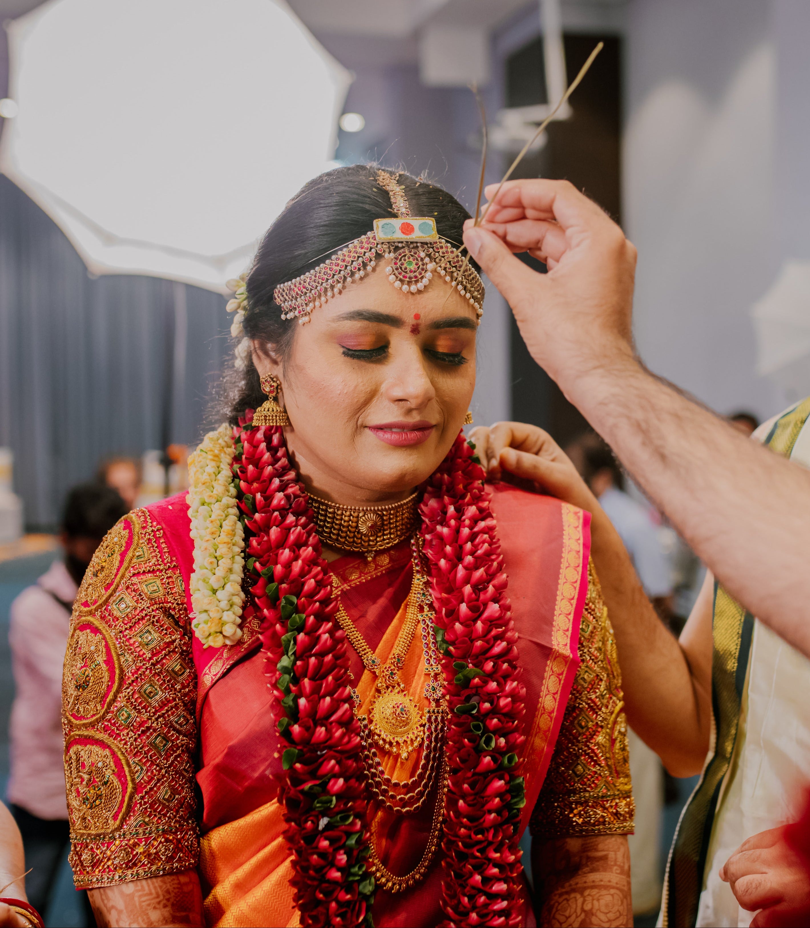 Bride Varshini in a handcrafted red silk blouse designed by Archana Karthick. She is in the middle of accepting blessings.