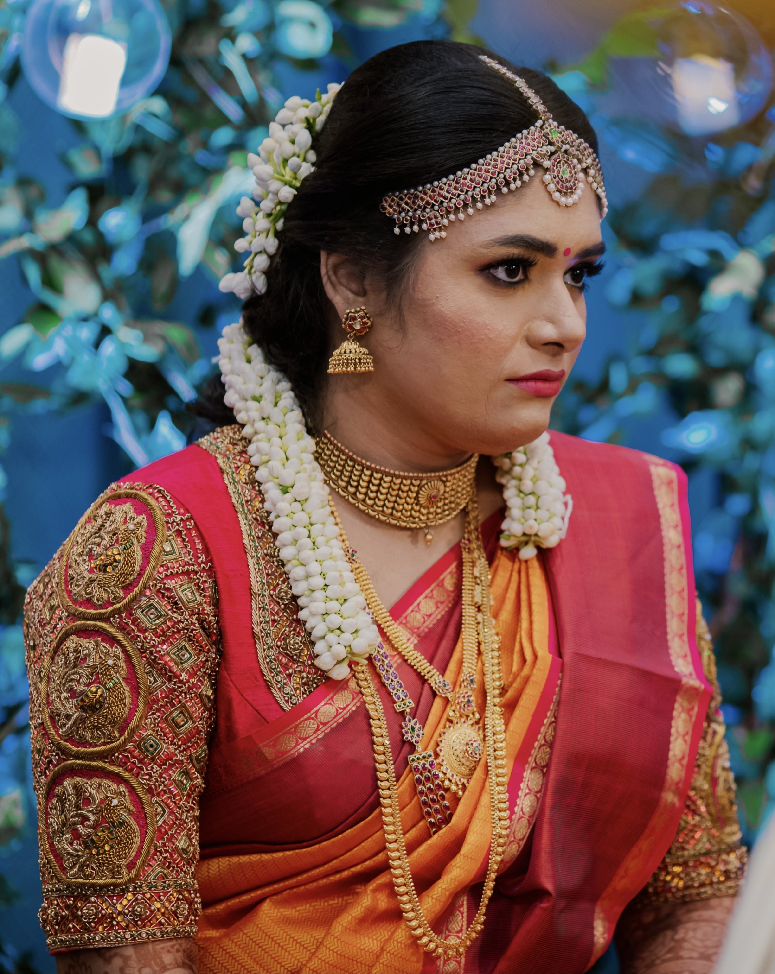 Bride Varshini in a handcrafted red silk blouse designed by Archana Karthick. She is looking away from the lens.