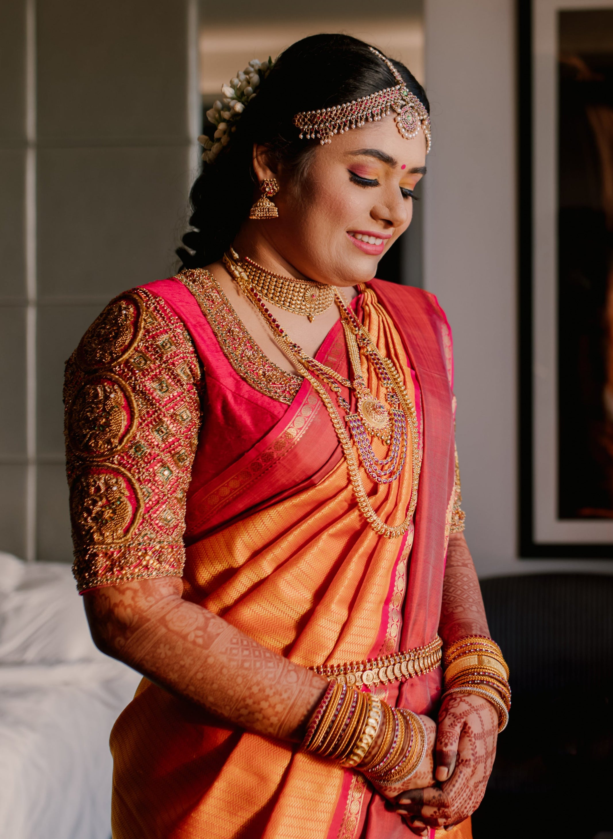 Bride Varshini in a handcrafted red silk blouse designed by Archana Karthick. She is looking down.