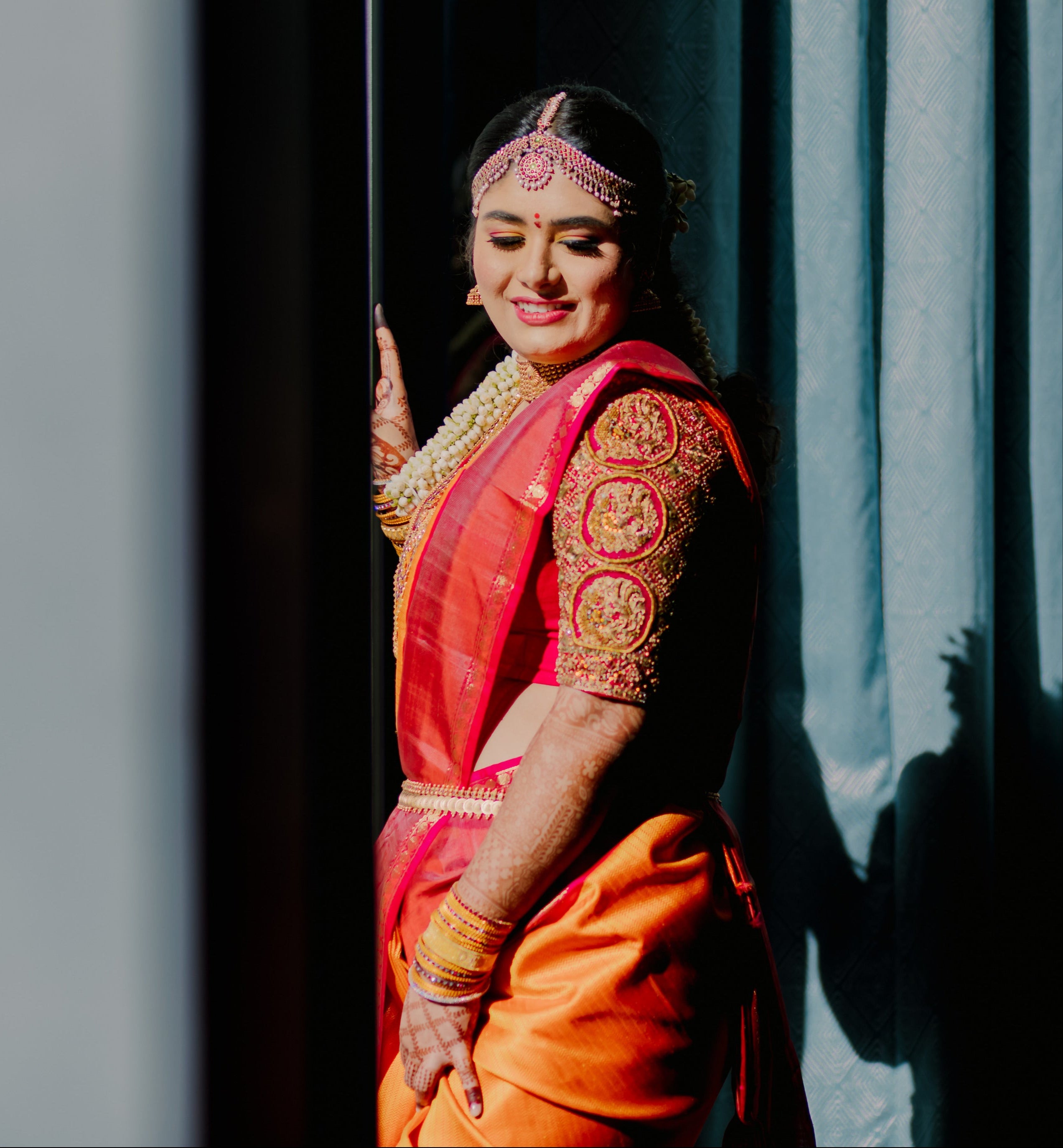 Bride Varshini in a handcrafted red silk blouse designed by Archana Karthick. She is posing in a way to highlight the sleeve.