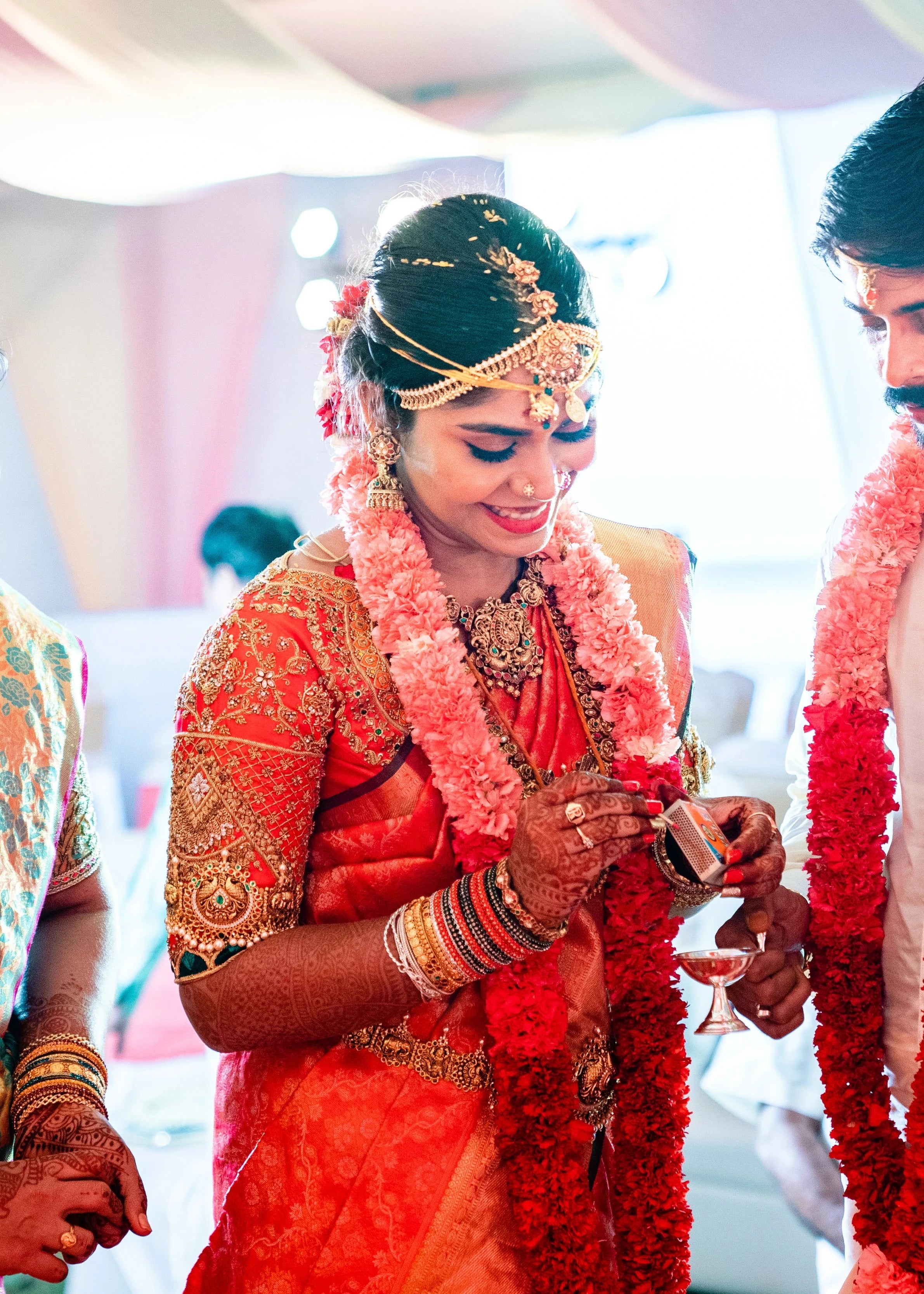 Bride Vidya D with garland in an orange silk blouse, handcrafted with beads, zardozi, kundan, resham, stones and zardozi by team Archana Karthick.