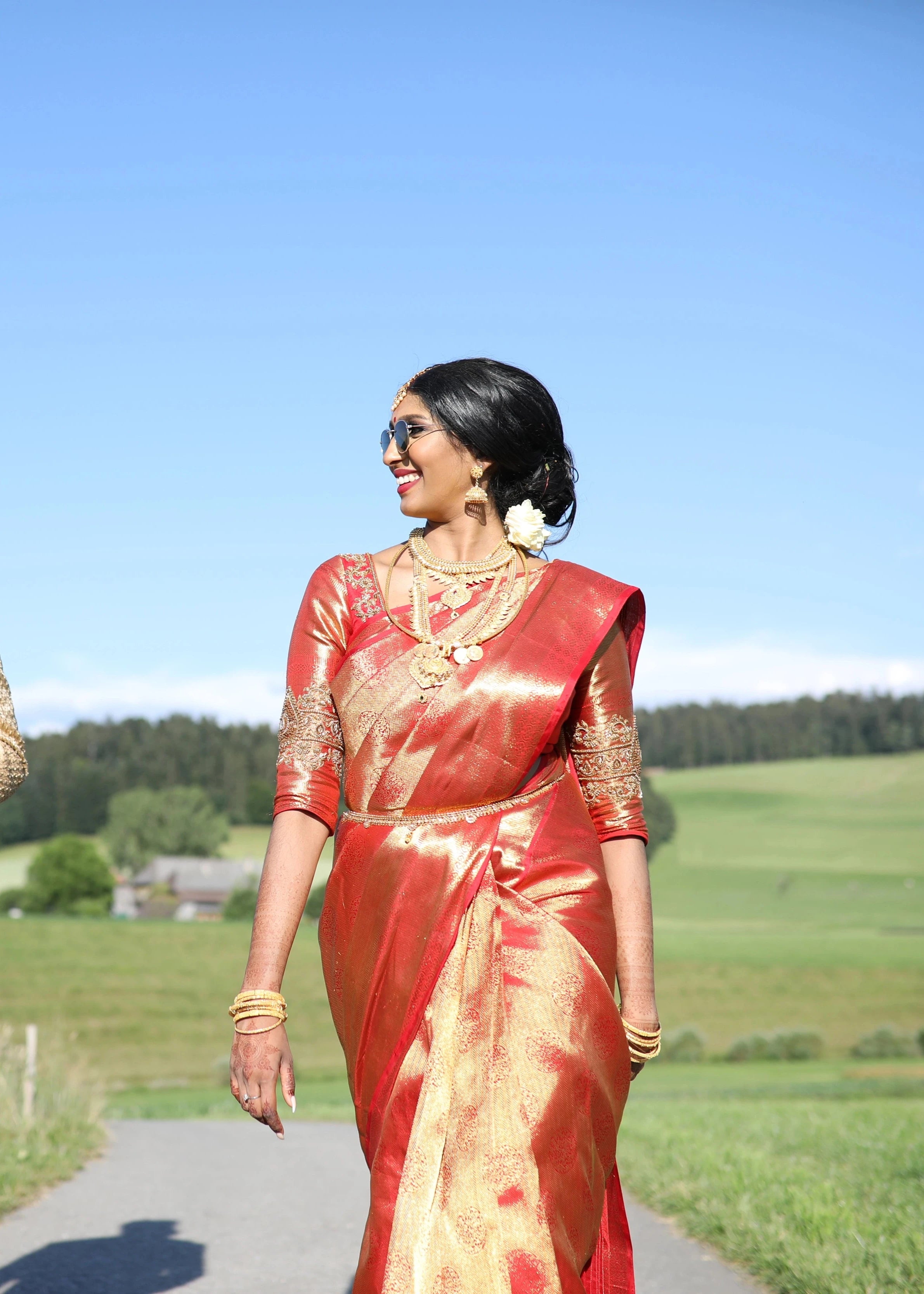 Bride Vithusika from Switzerland smiling with sunglasses in a red silk concept blouse for her wedding, handcrafted with zardozi, beads, sequins and cutdana by team Archana Karthick.