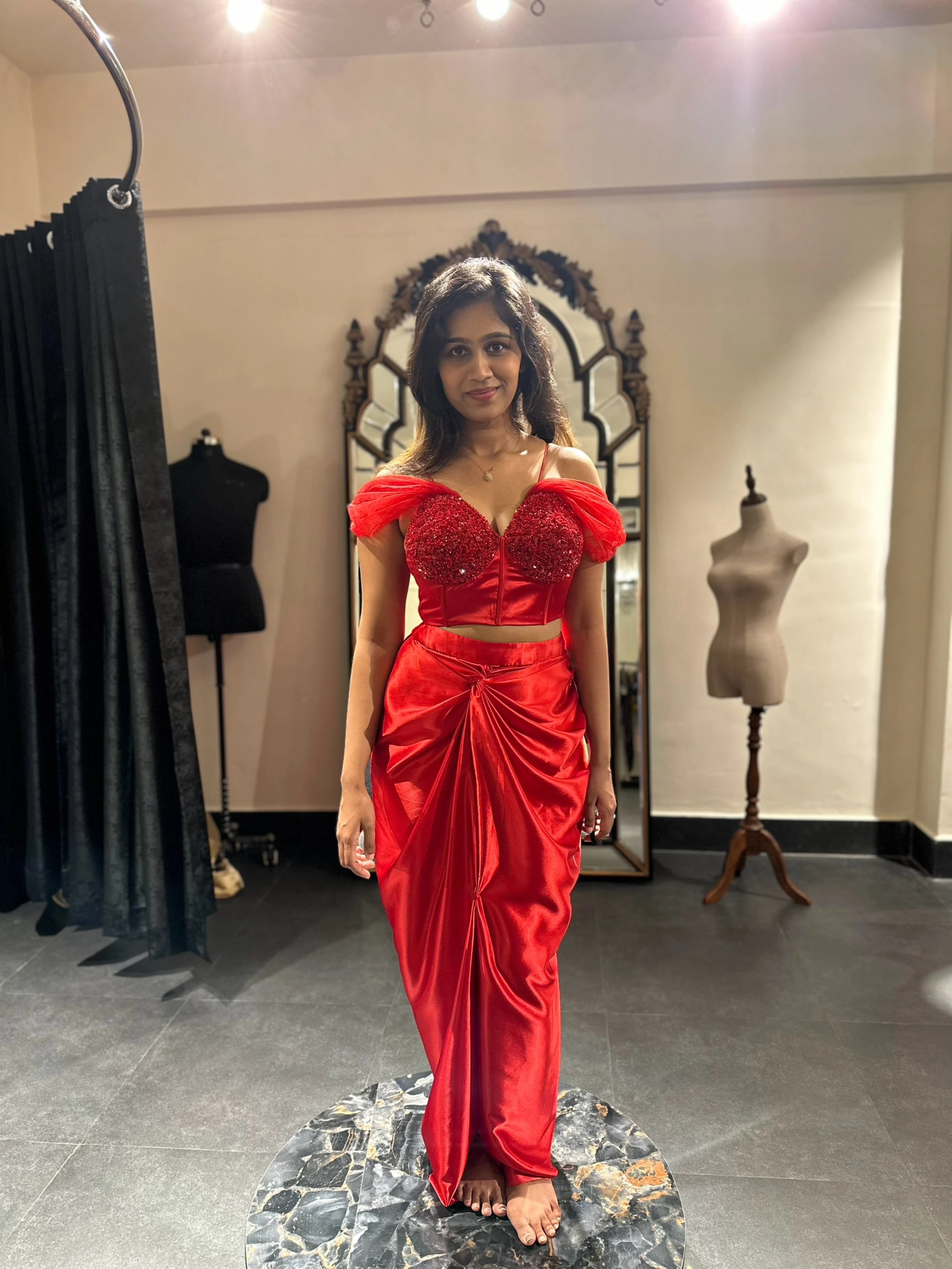 Bride for cocktail party in a red satin silk draped skirt and corset by team Archana Karthick.