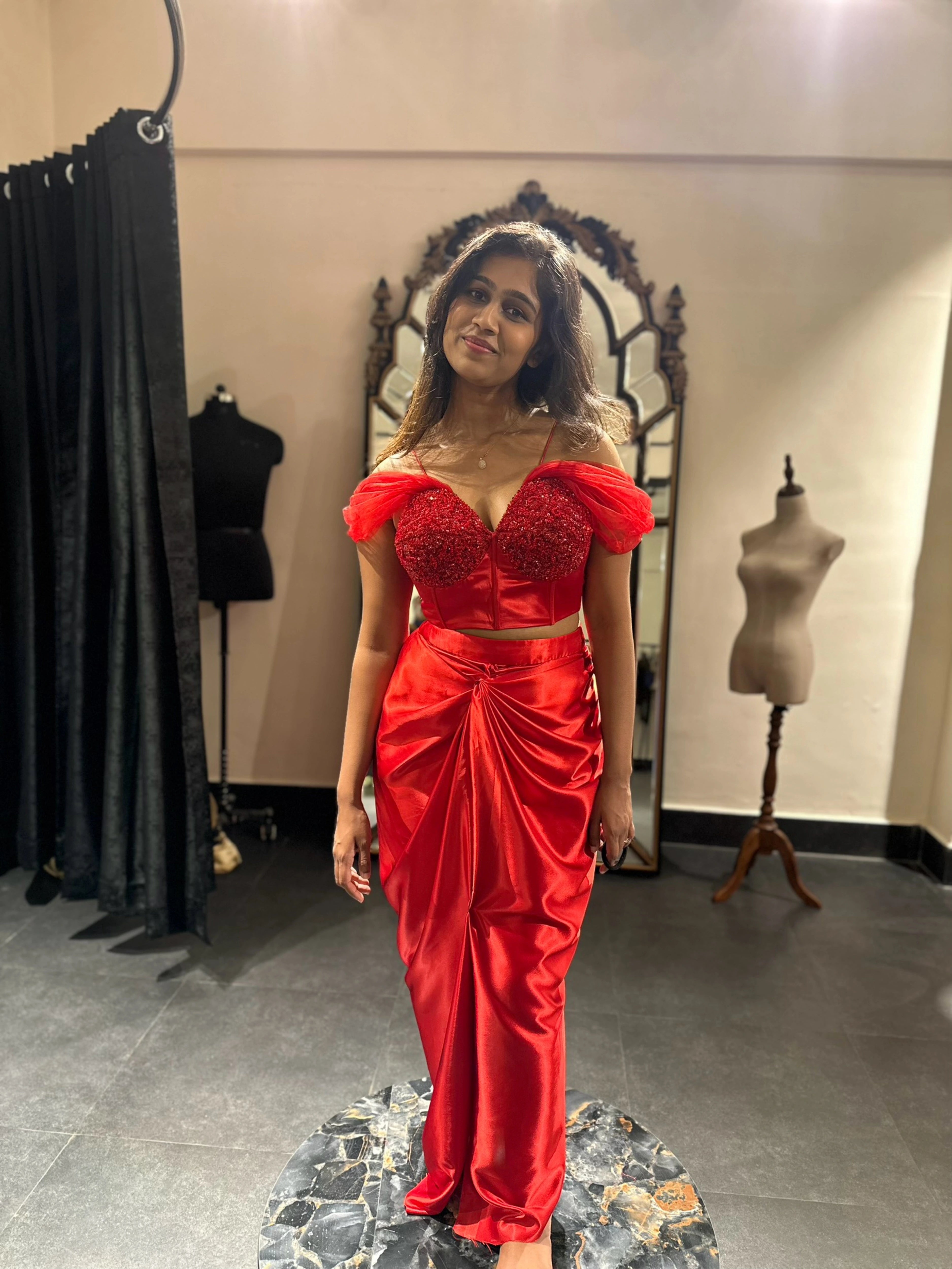 Bride for cocktail party, posing in a red satin silk draped skirt and corset by team Archana Karthick.
