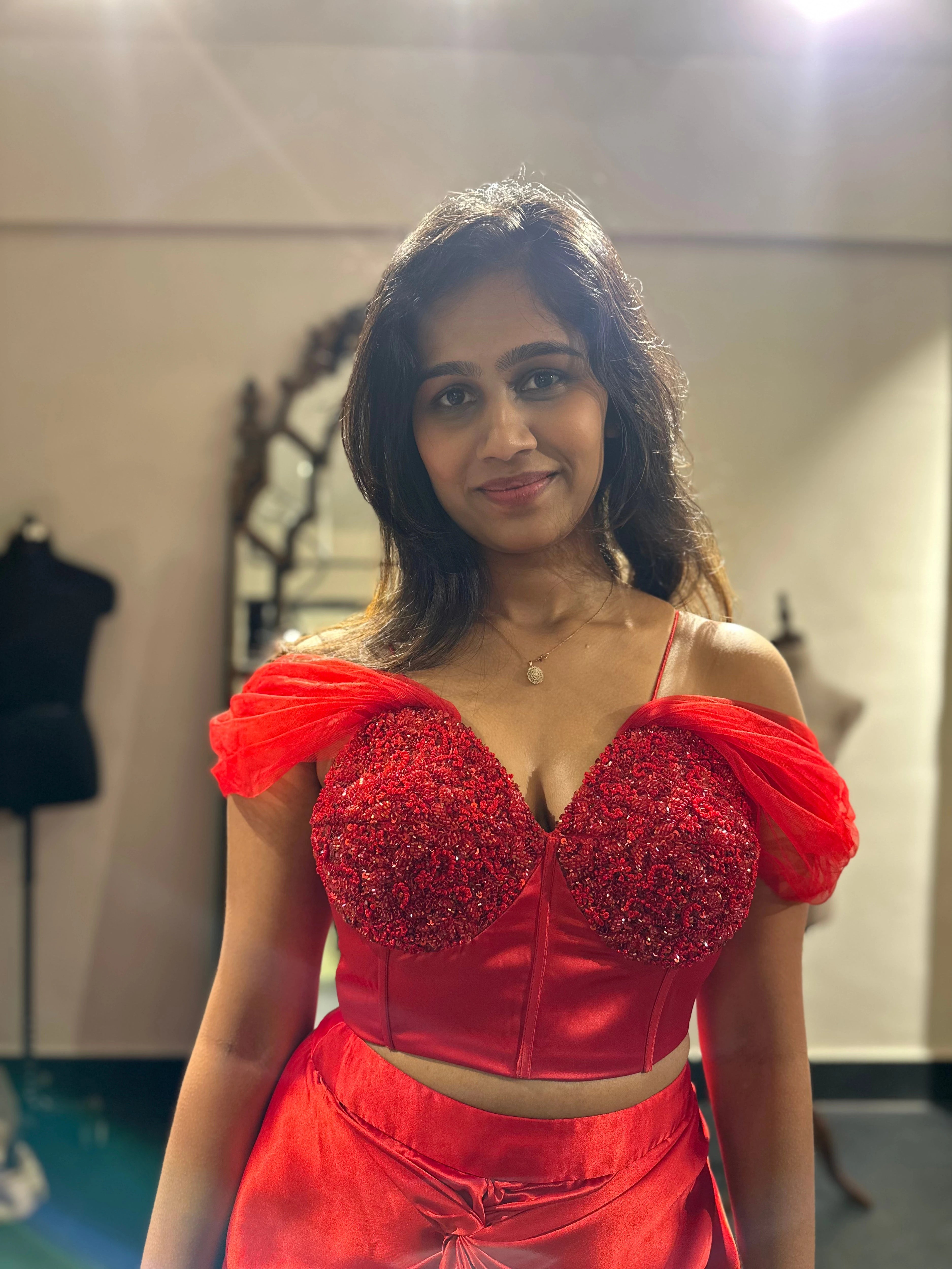 Bride for cocktail party, smiling in a red satin silk draped skirt and corset by team Archana Karthick.